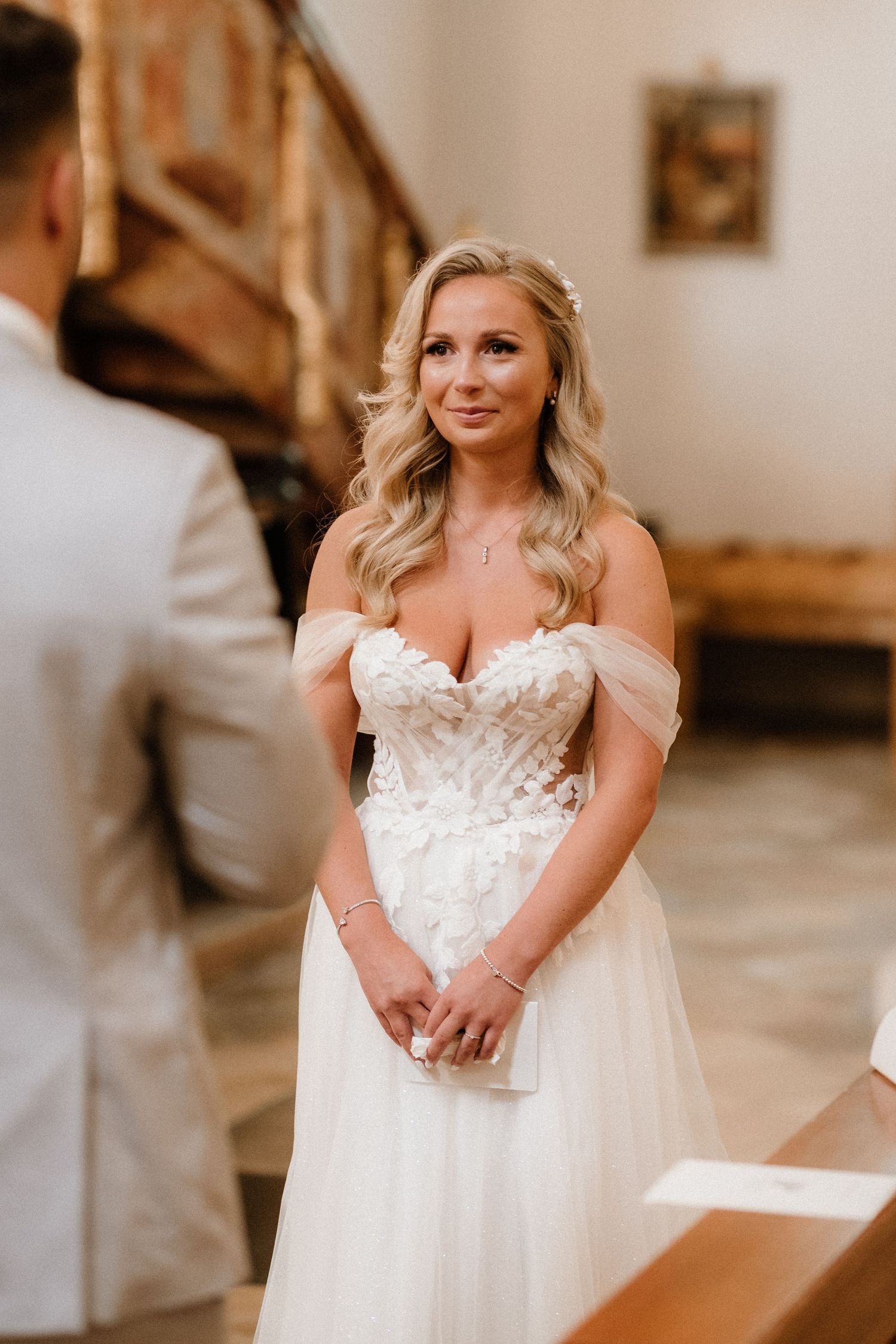 Bride in an off-shoulder lace wedding gown stands at the church altar.