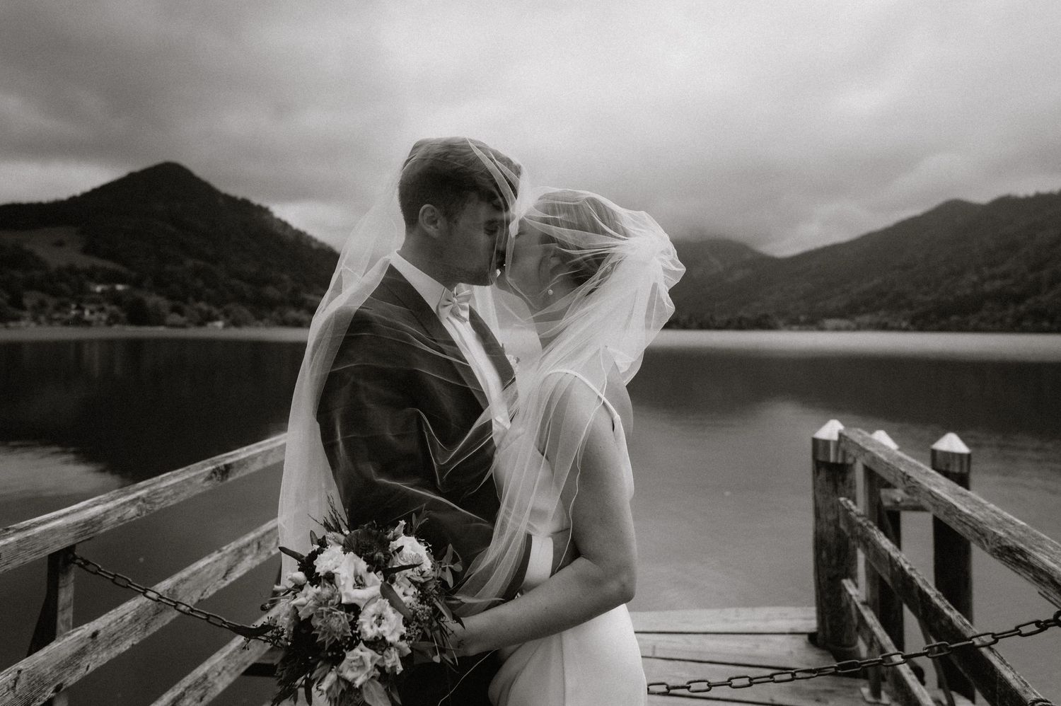 Wedding couple embracing on a dock with mountains and lake in the background.