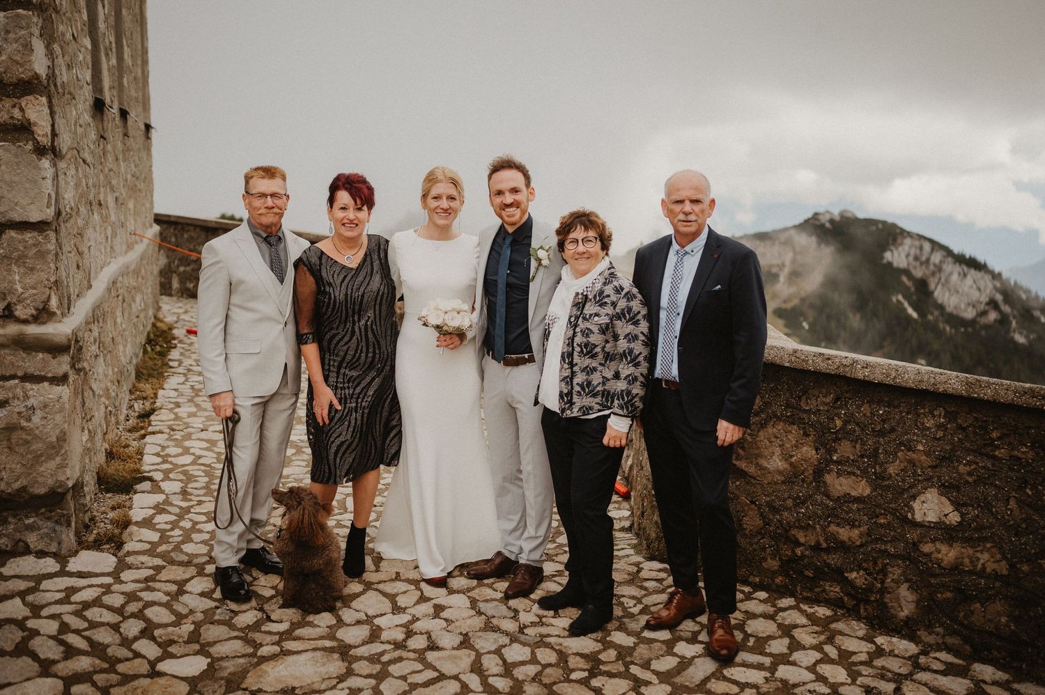 Wedding party group photo on a stone terrace with mountain views in the background.