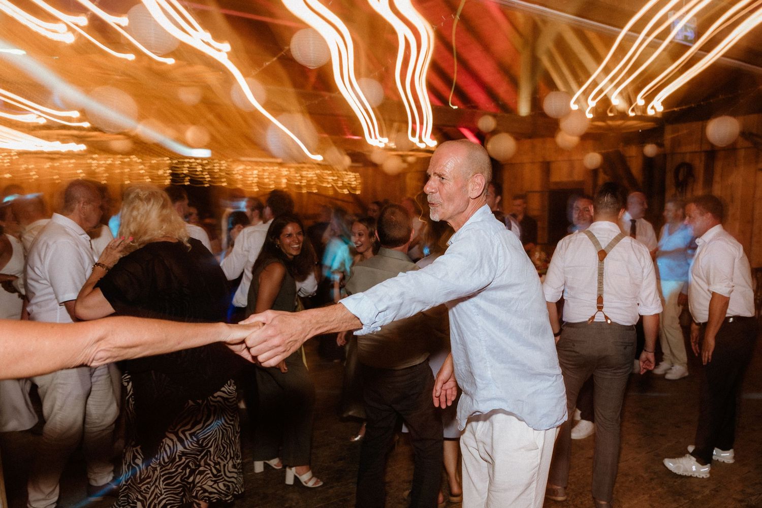 Energetic dance party with guests moving under warm lighting in a rustic barn venue.