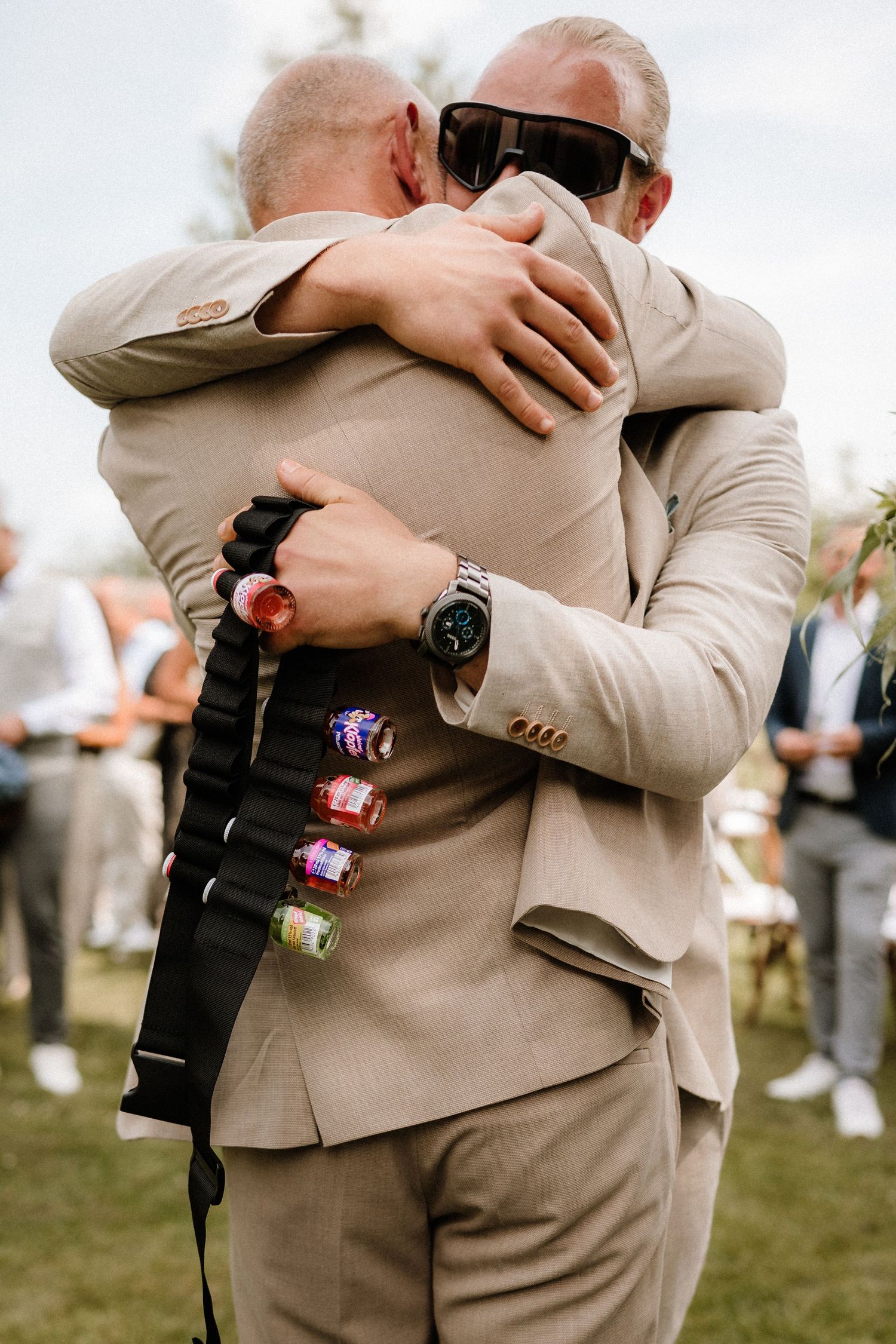 Close-up of groomsmen wearing tan suits with colorful shot holders attached to their belts.