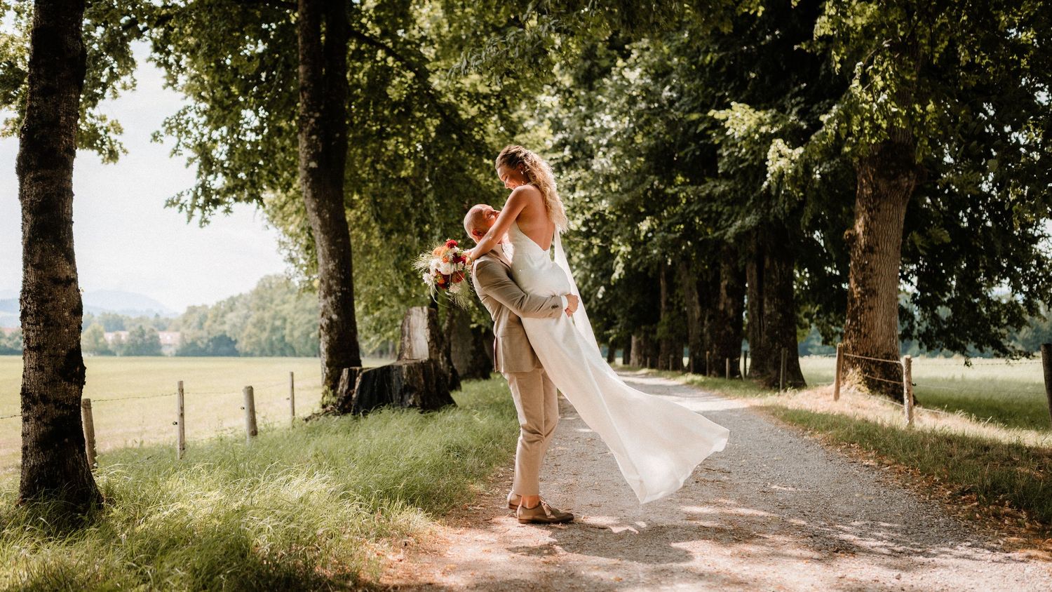 Panoramic view of a tree-lined path where a wedding couple shares intimate moments.