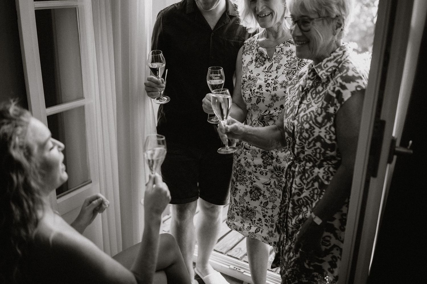 Black and white photo of people sharing drinks and conversation by doorway.