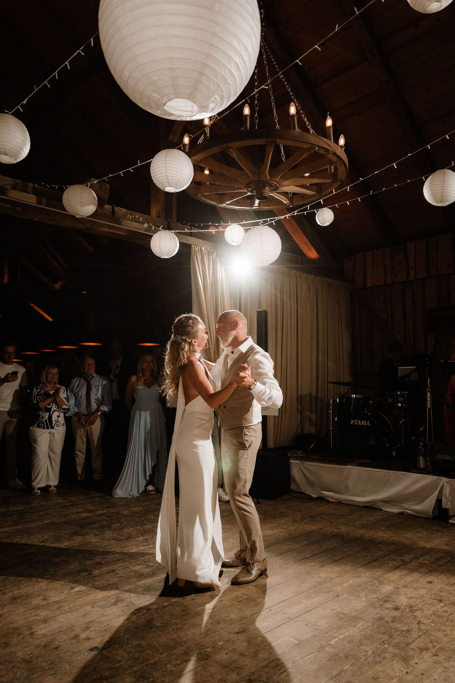 Couples dancing beneath white paper lanterns in a dimly lit rustic barn setting.