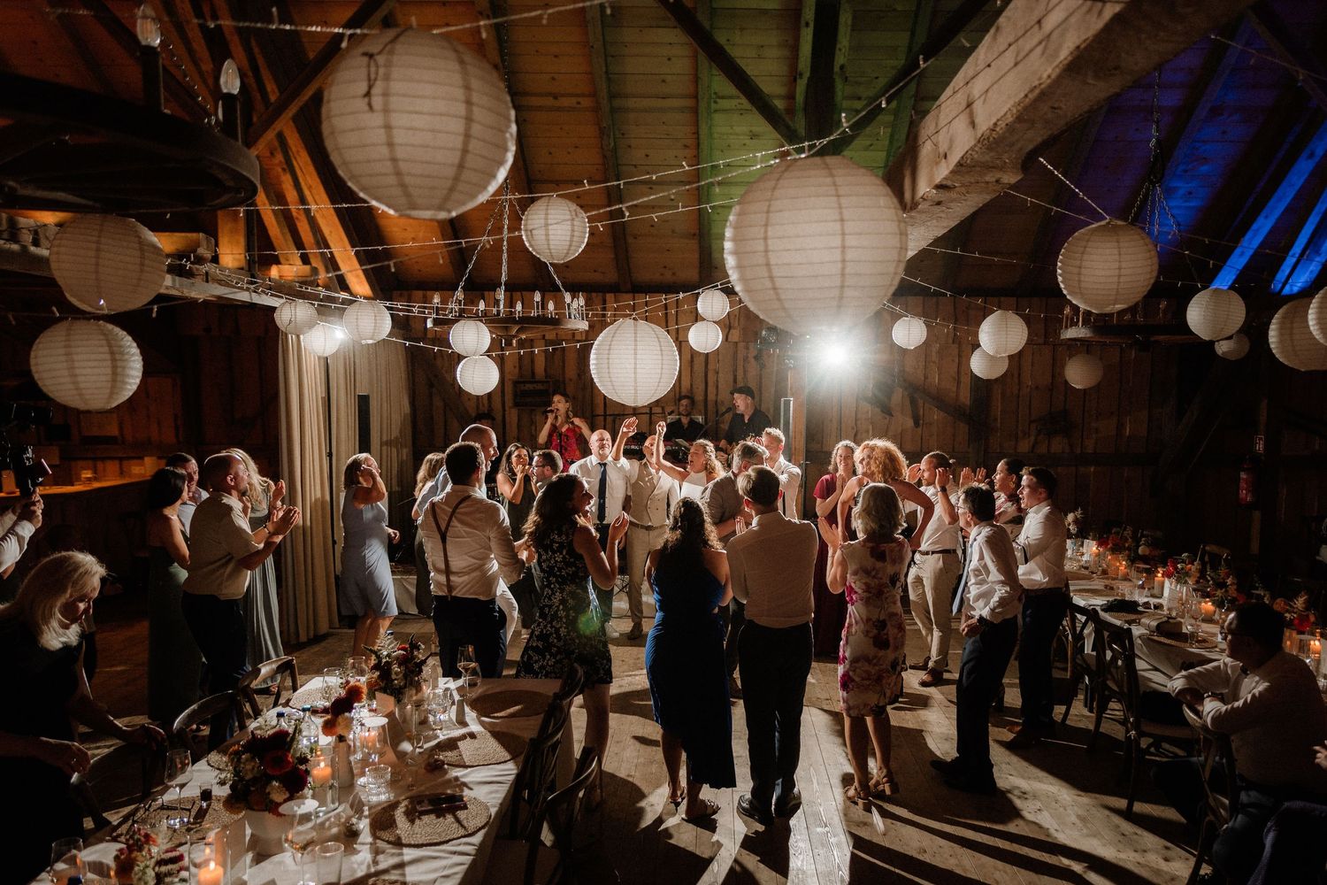 Wedding reception venue decorated with white paper lanterns and guests mingling on dance floor.