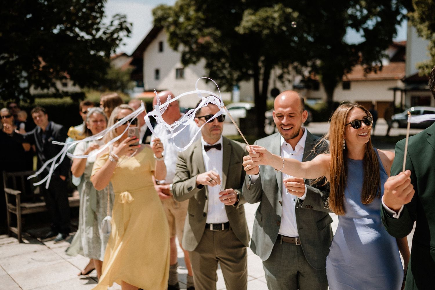 Wedding party and guests celebrating outdoors with raised hands and joyful expressions.