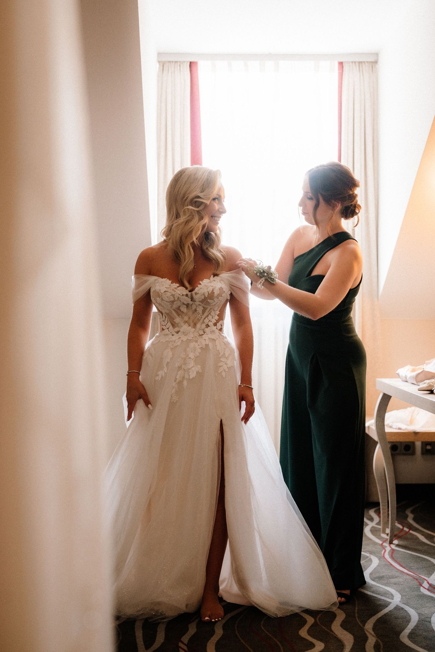 Wedding preparations show bridesmaids in dark dresses helping with a flowing white gown.