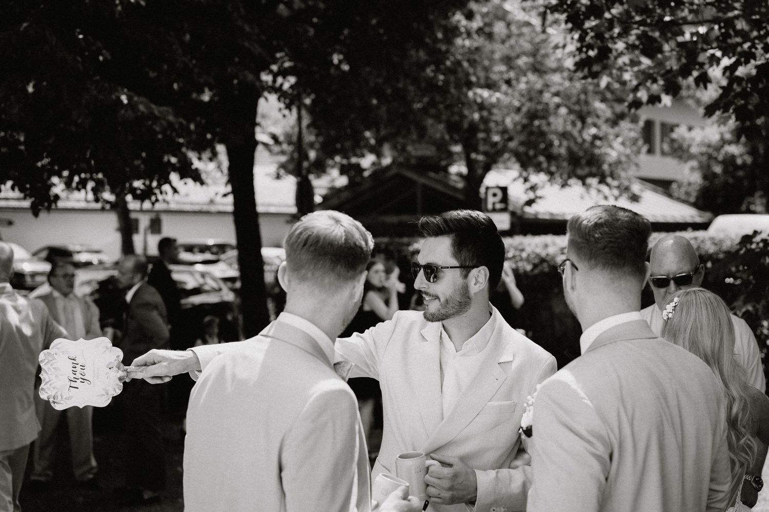 Guests mingling at an outdoor celebration under trees on a sunny day.