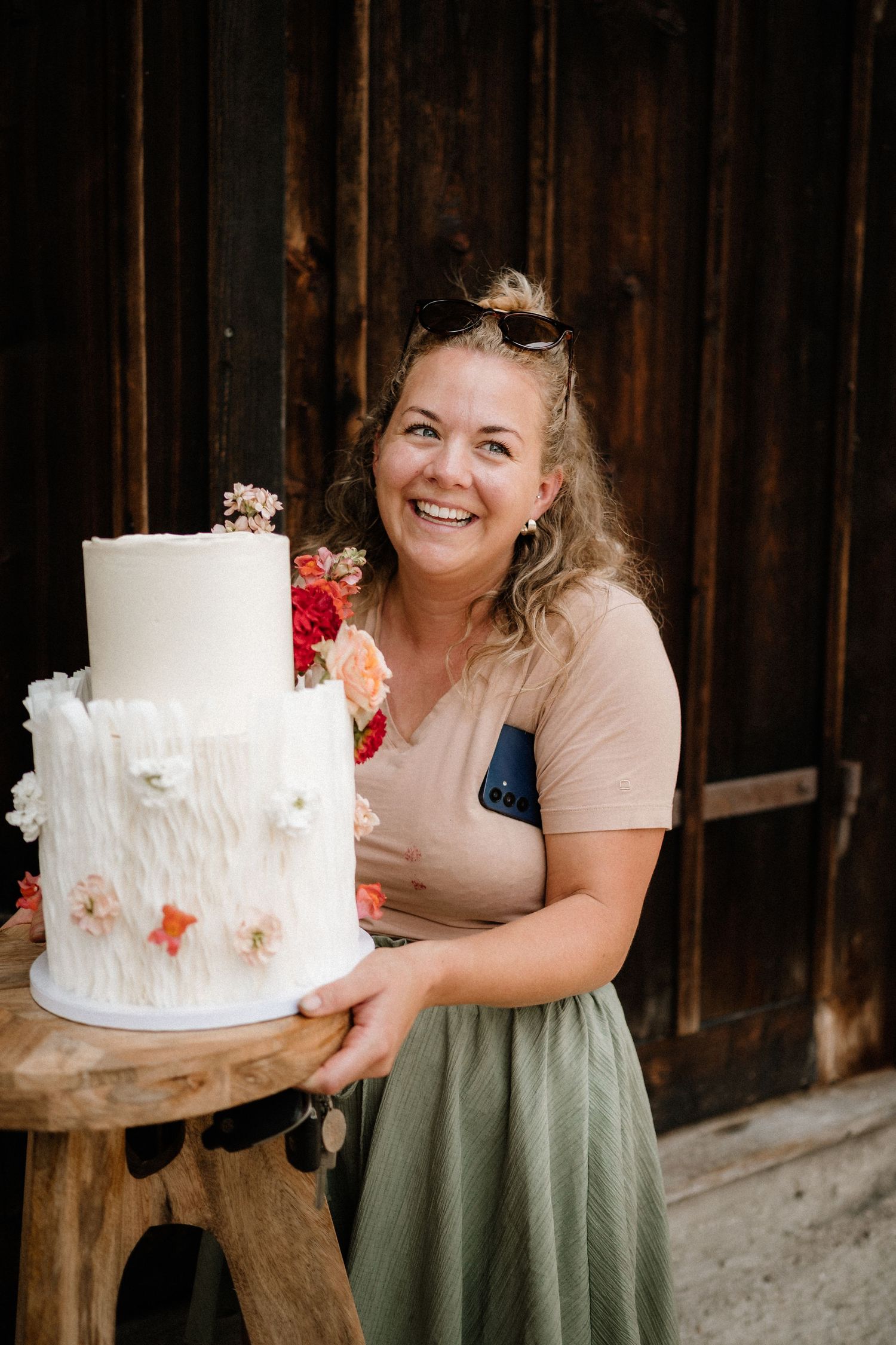 Wedding cake with textured frosting and red floral accents displayed at a rustic venue.