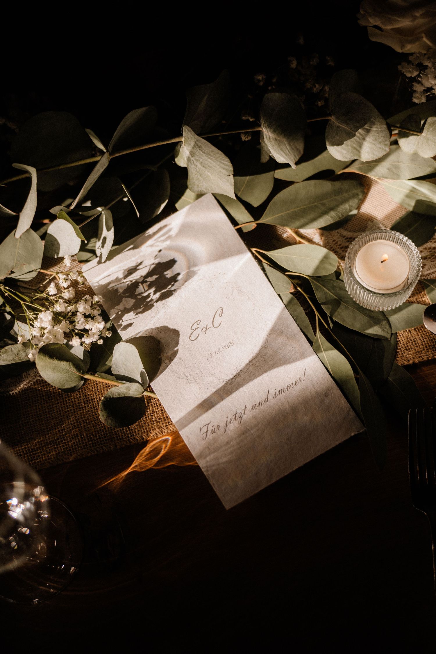 Elegante Hochzeitsplatzkarten mit Kalligraphie zwischen Eukalyptusblättern und Kerzenlicht in einer romantischen Umgebung. Dama Fotografie