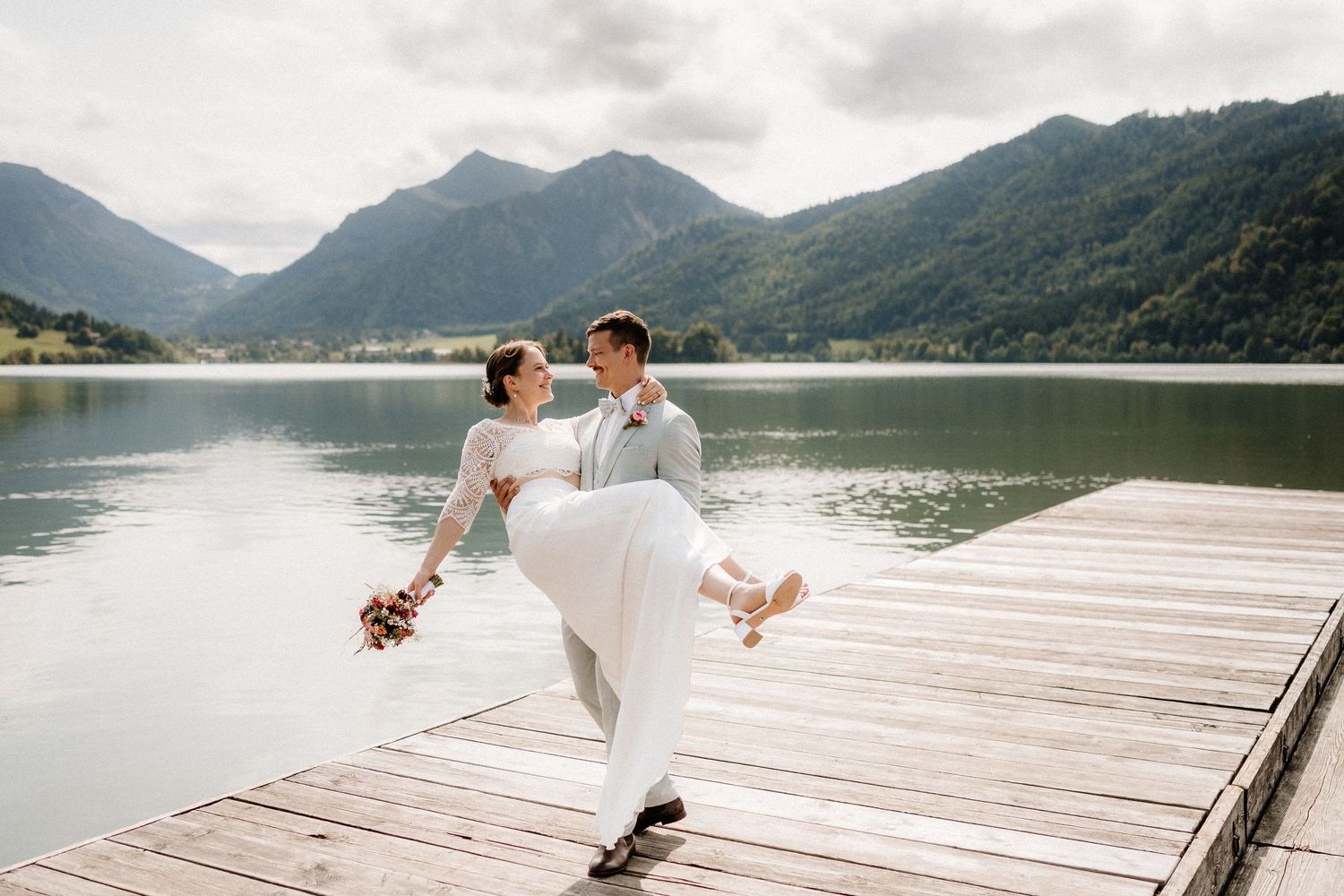 A couple shares romantic moments on a wooden dock overlooking a serene mountain lake.
