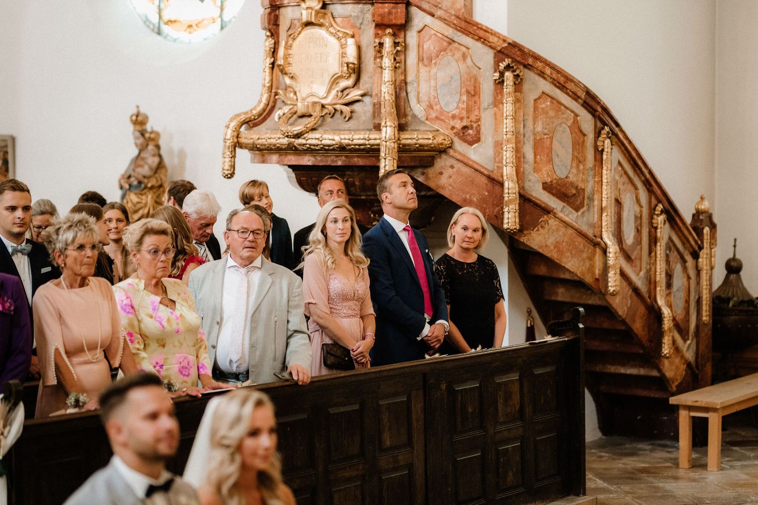 Wedding guests seated in historic church pews with ornate wooden details.