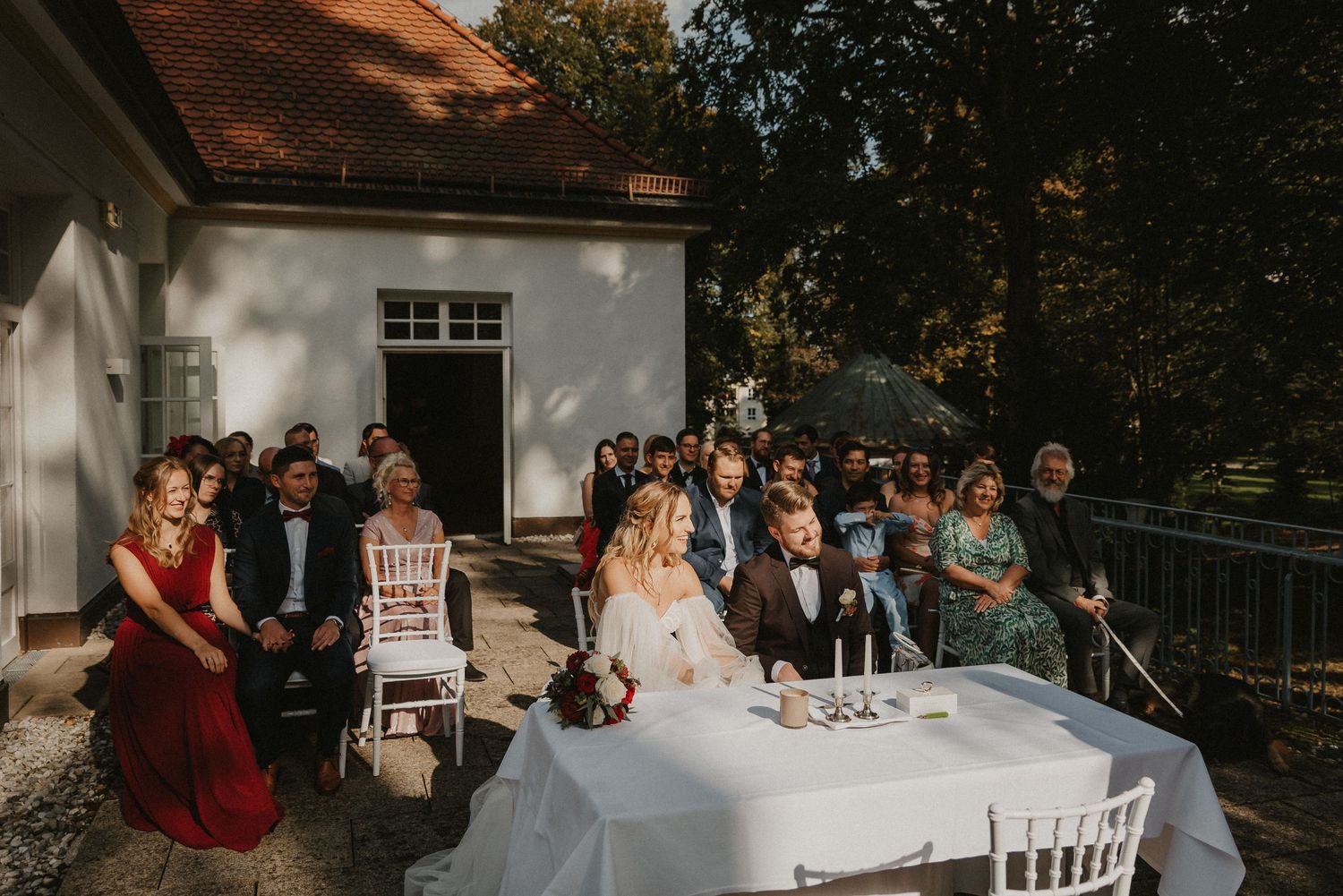 Panoramic view of outdoor wedding venue with white chairs and guests during ceremony.