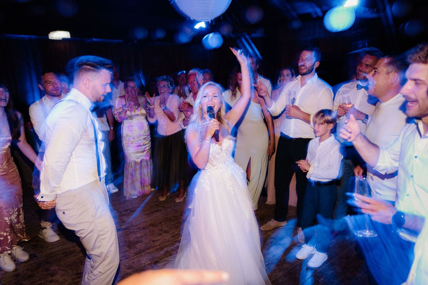 Wedding guests dancing and having fun under dramatic blue party lighting.