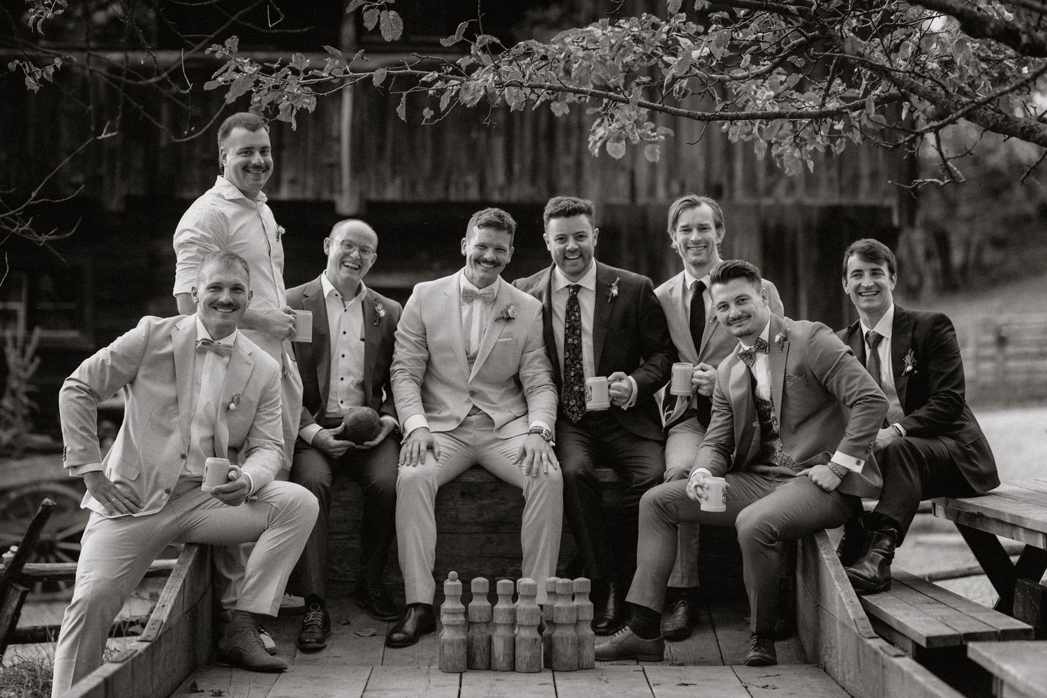 Group of friends sitting outdoors on wooden deck with drinks, laughing and enjoying themselves.