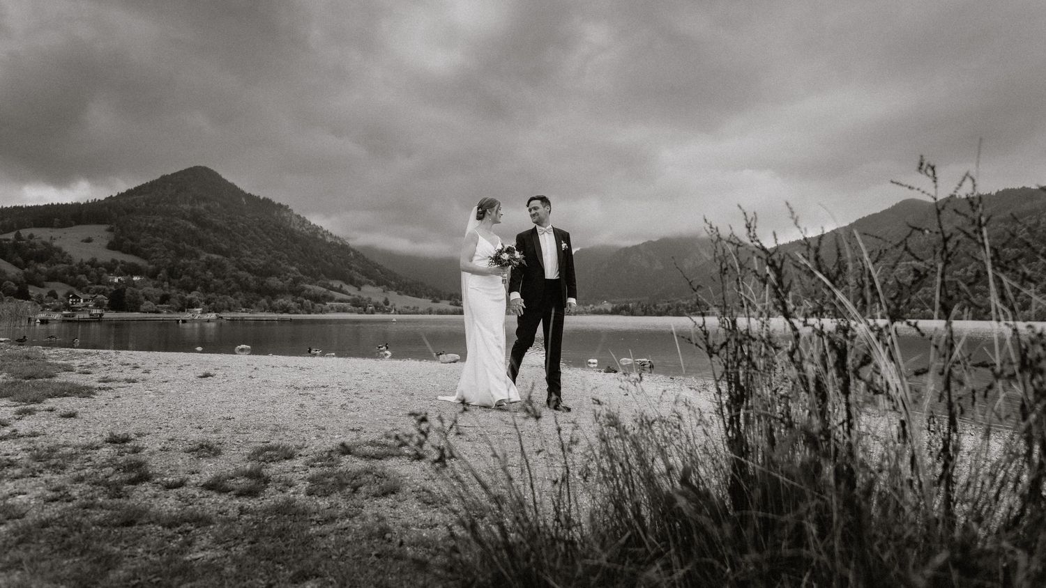 Wedding couple silhouetted against dramatic mountain lake landscape.