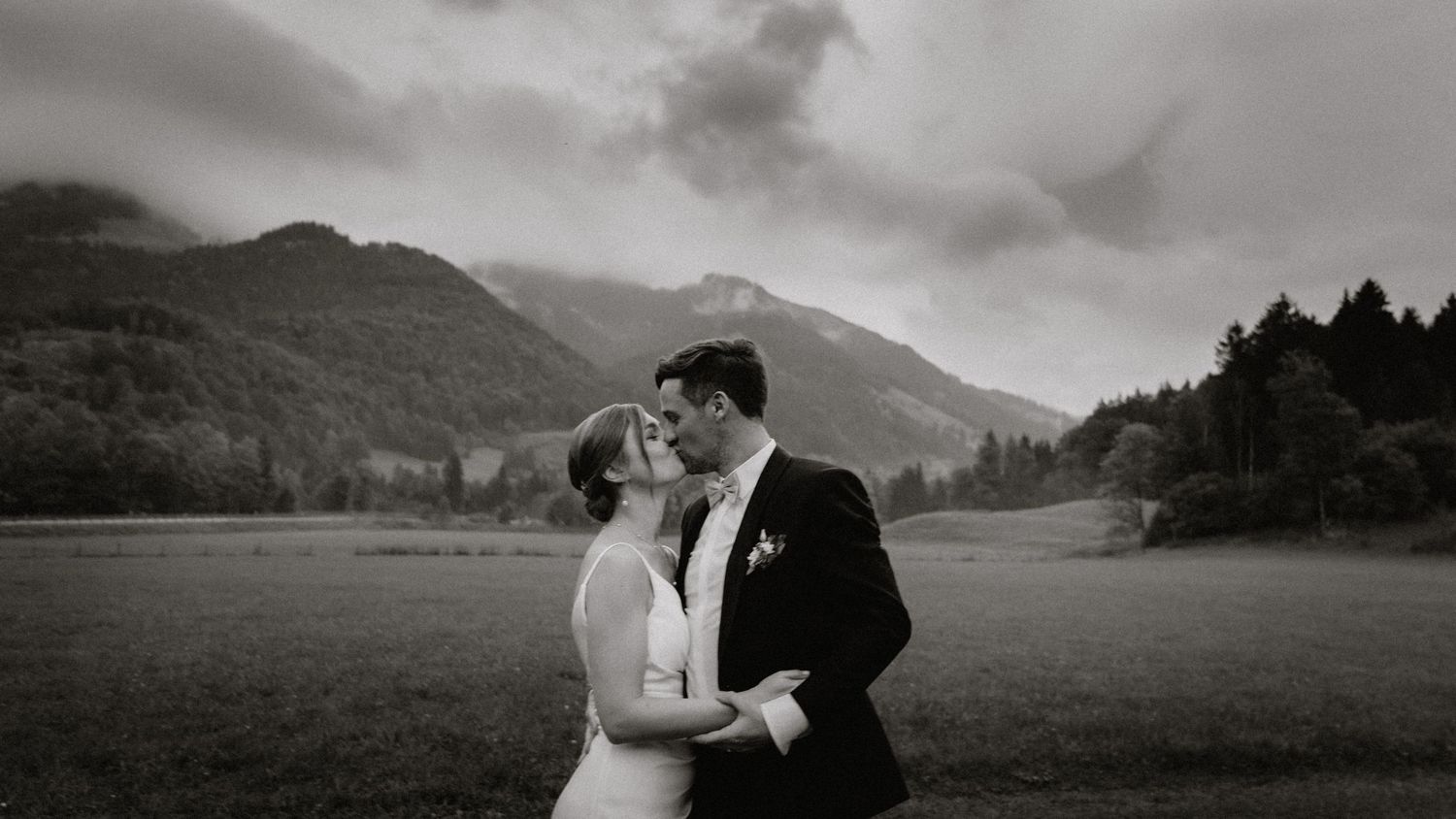 Romantic wedding couple poses in front of misty mountain landscape at sunset.