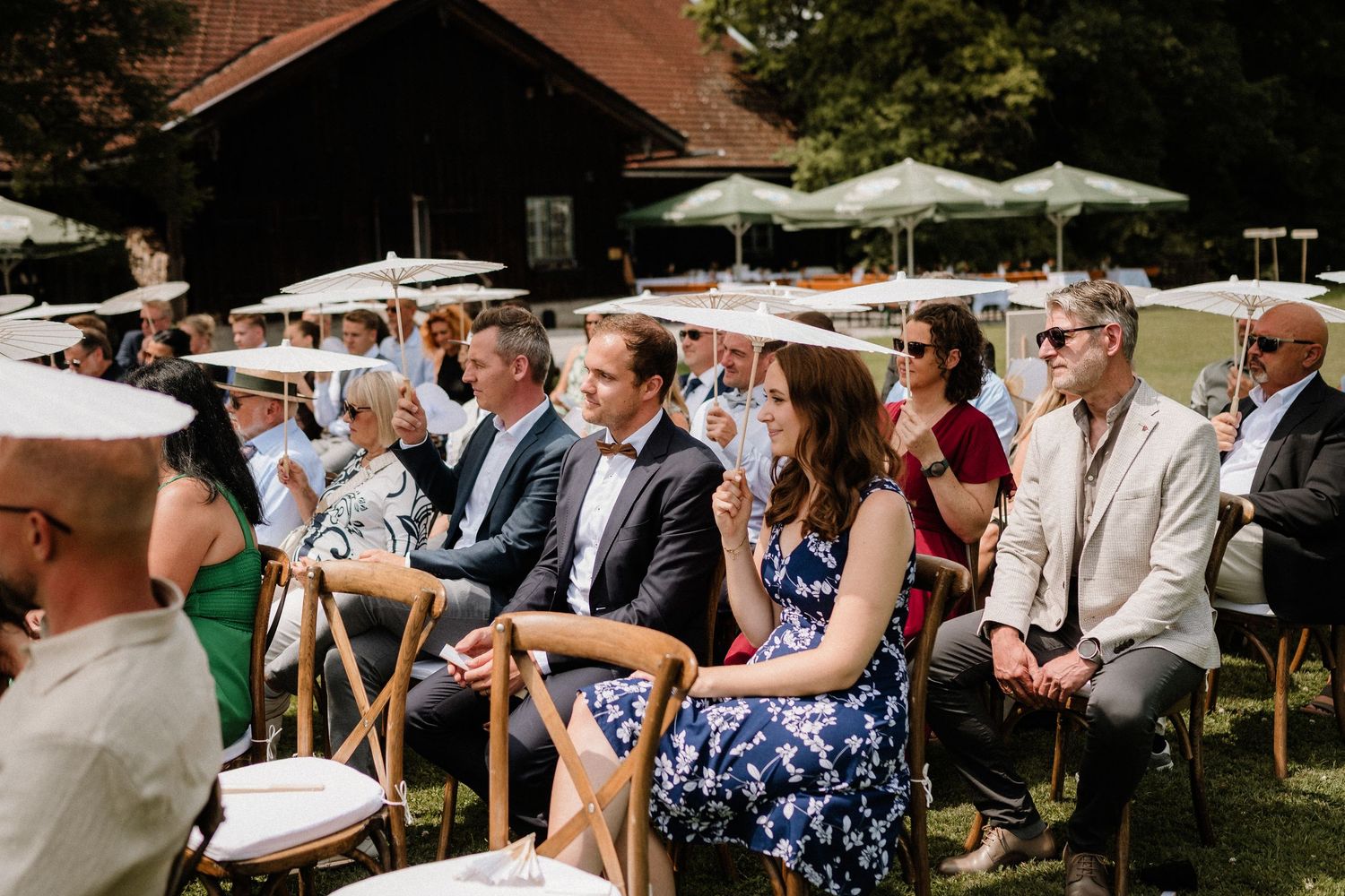 Wedding guests seated under white umbrellas at an outdoor ceremony.