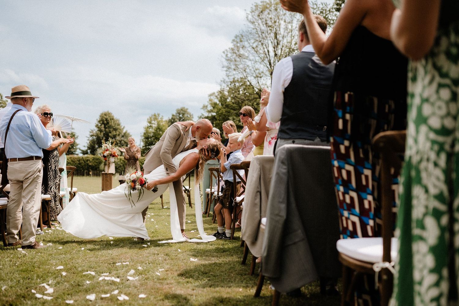 Wedding guests seated in rows during an outdoor ceremony with scattered flower petals.