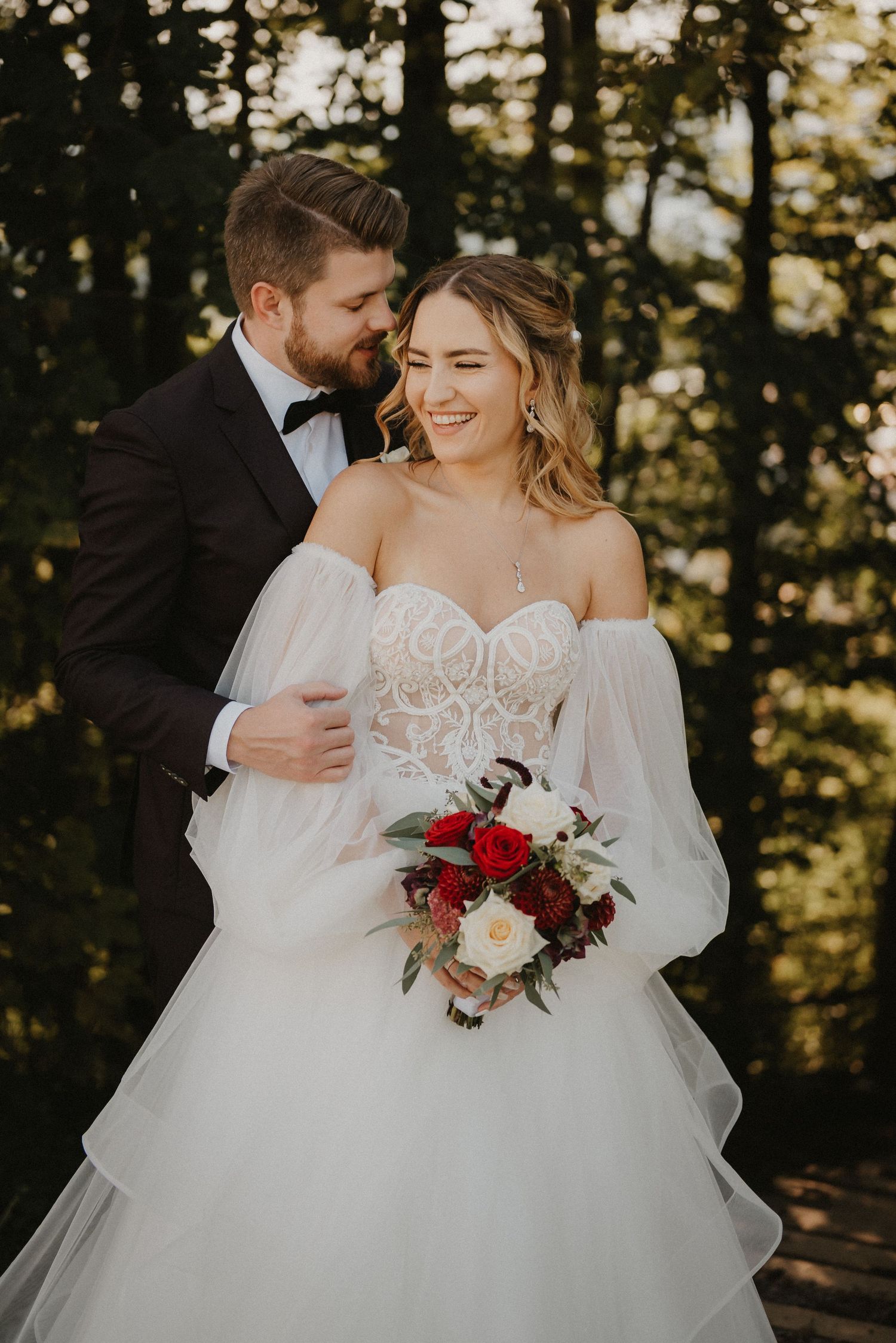 Ein fröhliches Hochzeitsporträt, das Lachen und Romantik bei natürlicher Außenbeleuchtung einfängt. Von Dama Fotografie Bad Tölz