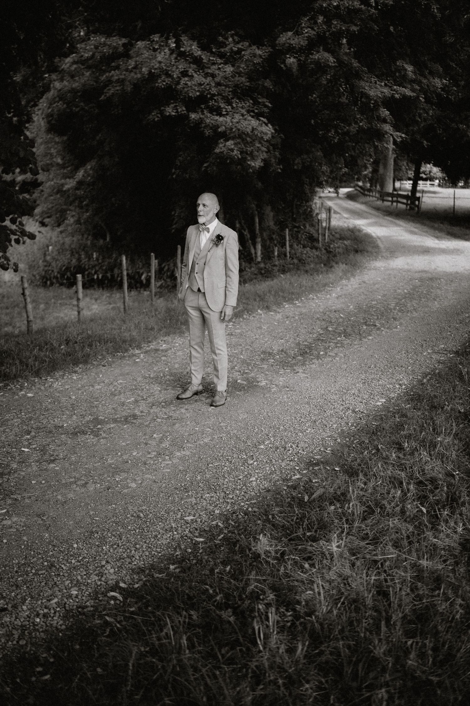 Black and white photo of person walking along a tree-lined gravel path.