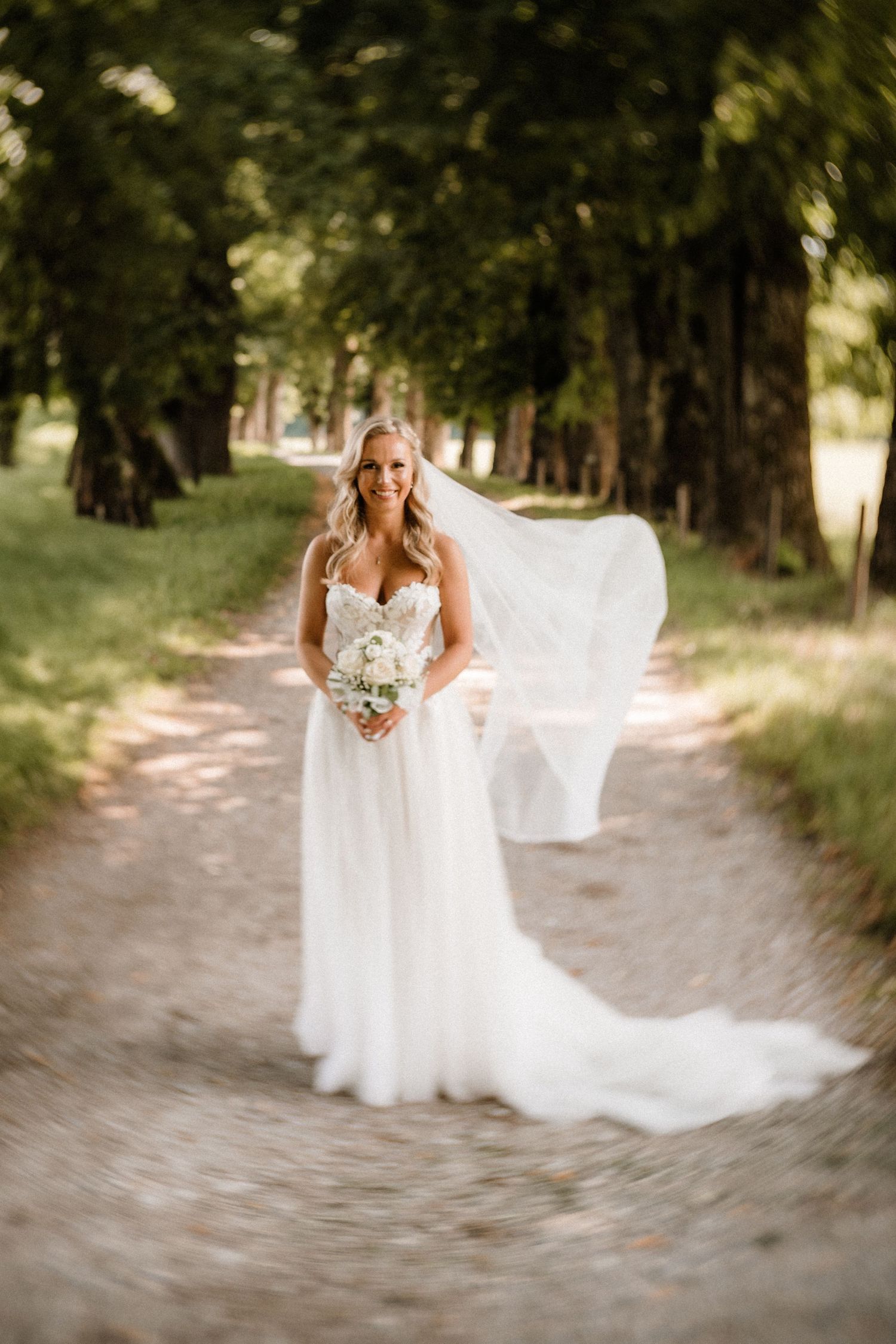 Ethereal bridal portraits on a sunlit forest path with flowing white gown.