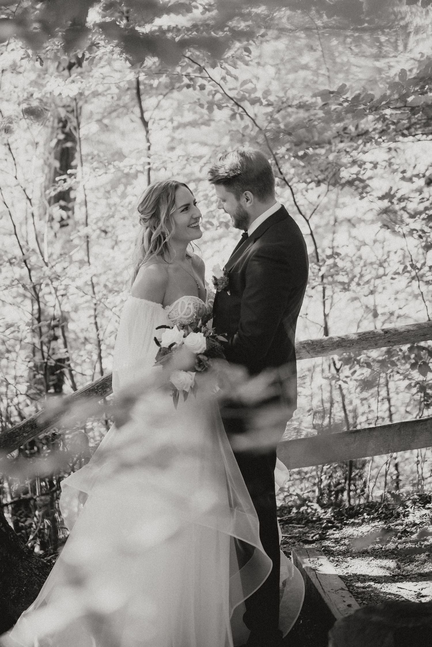 Artistic black and white wedding photography with natural light filtering through trees.