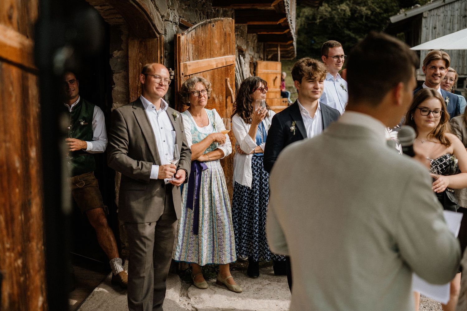 Wedding guests socializing in formal attire at a rustic wooden venue.