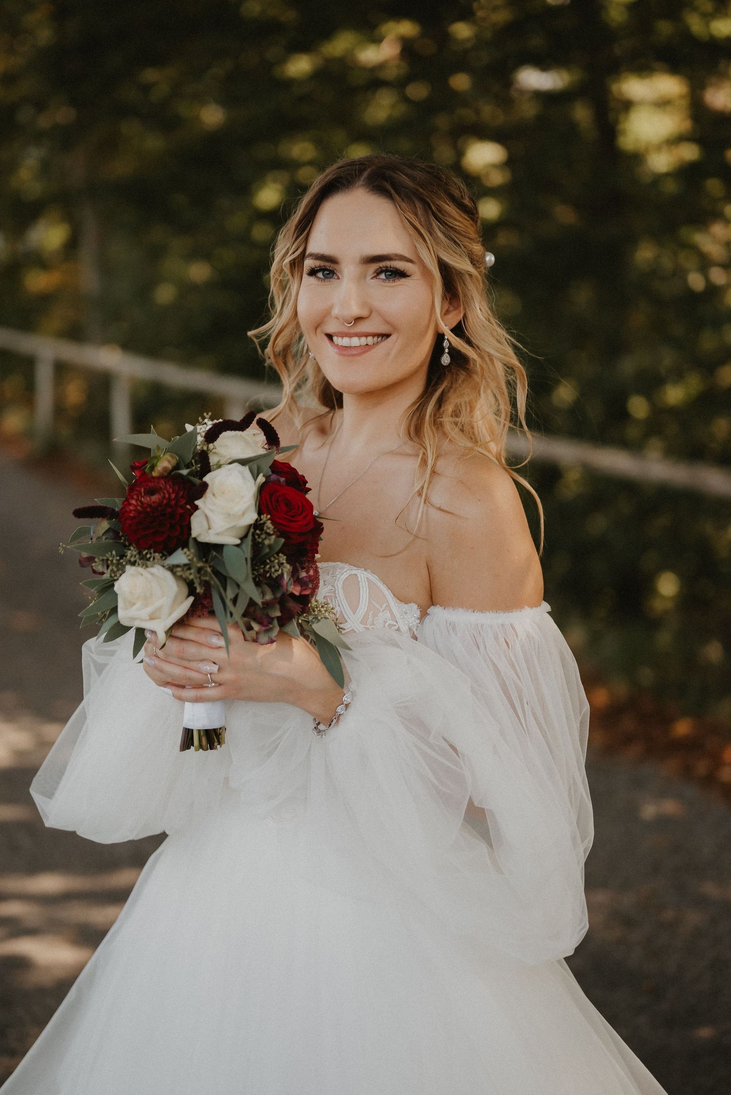 Bride in an off-shoulder wedding dress holding a red and white rose bouquet.