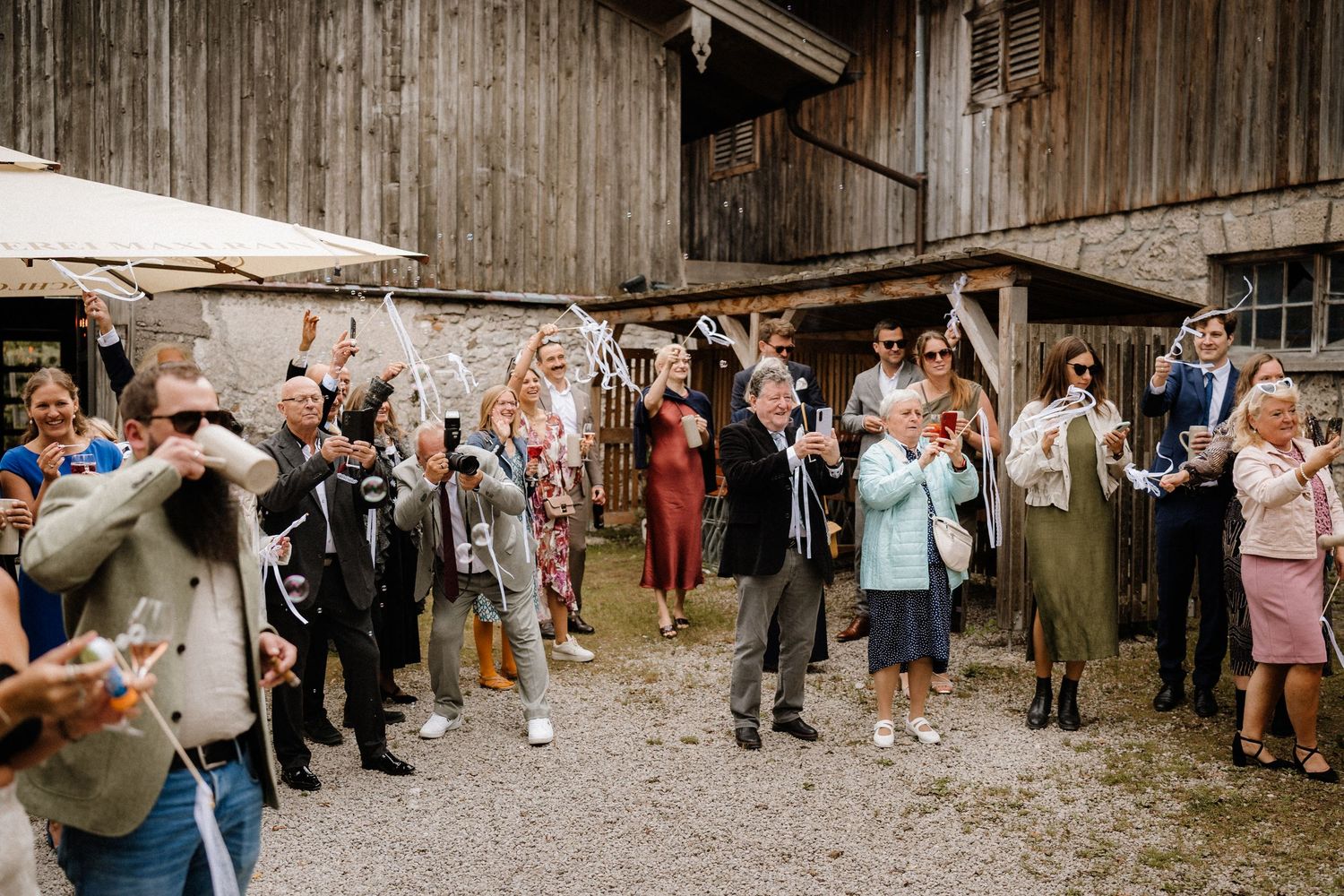 Wedding guests cheer and celebrate outside a rustic wooden barn venue.