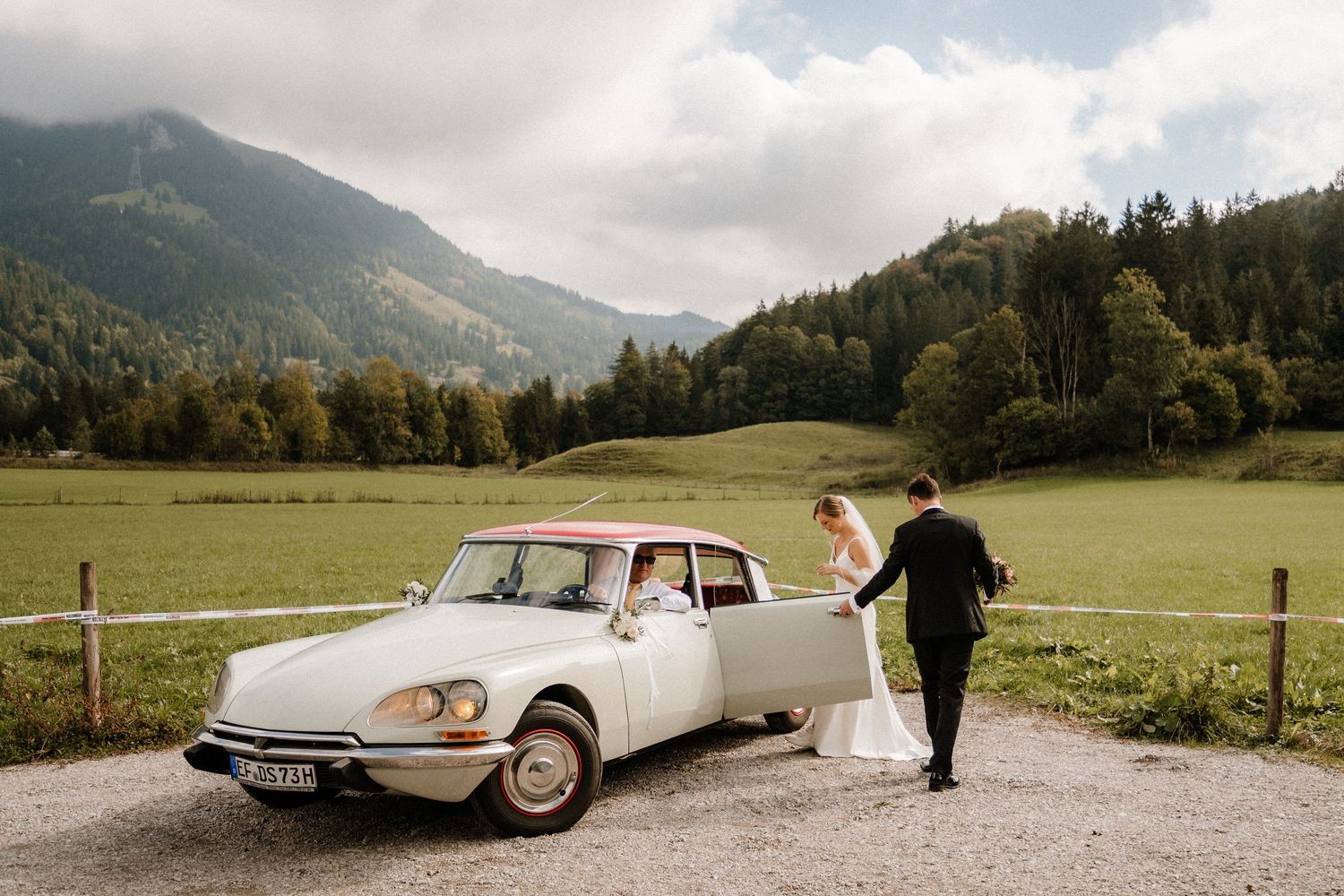 A classic white vintage car sits parked in a scenic mountain landscape.