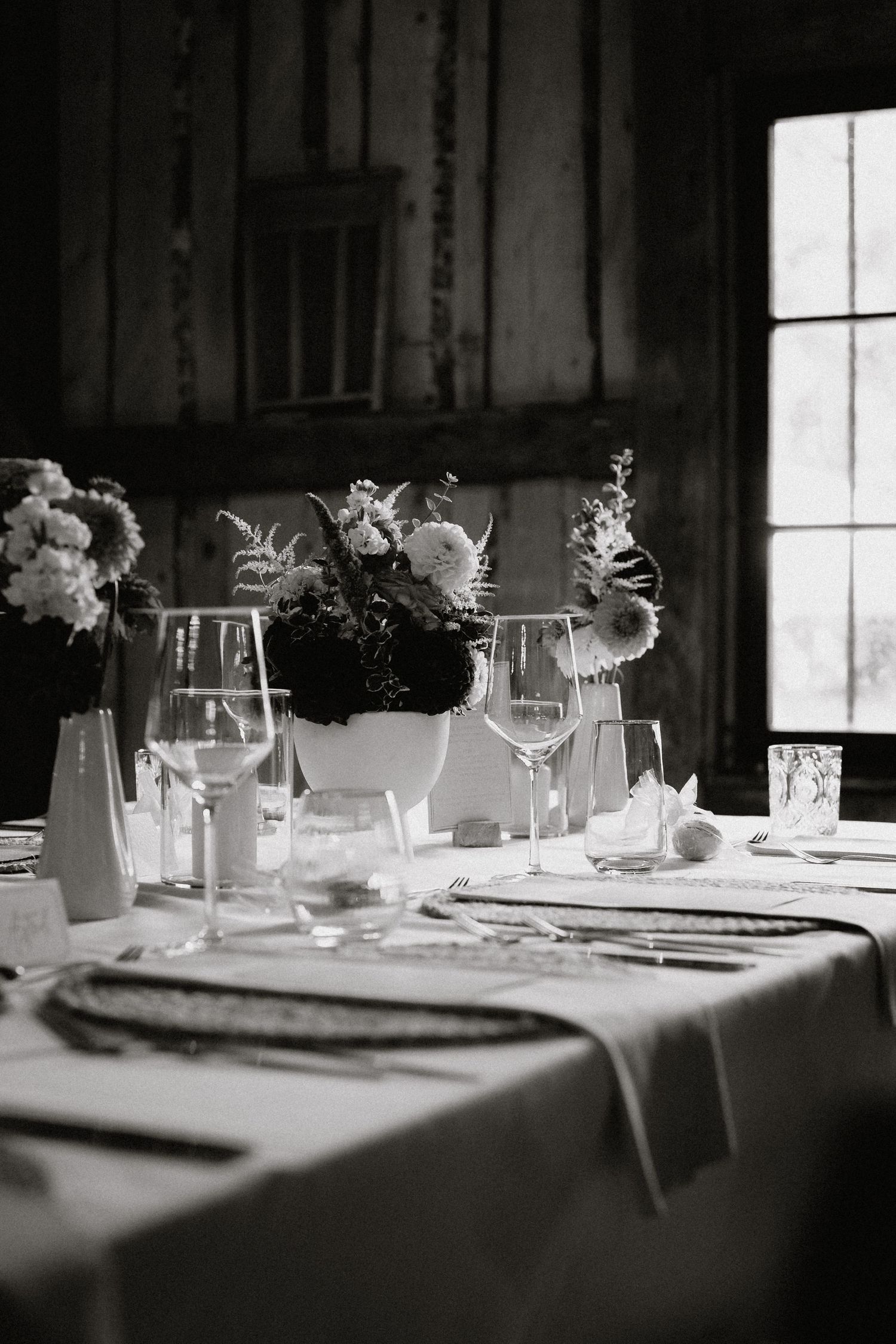 Delicate floral centerpieces in glass vases line a rustic dining table.