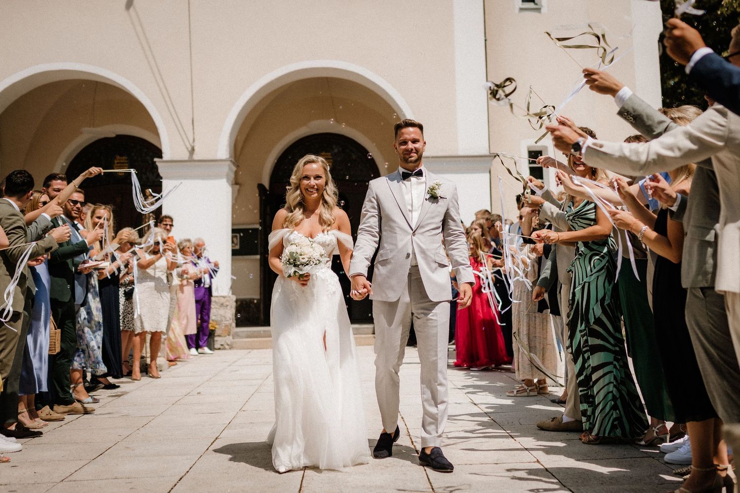 Wedding party walks through a beautiful colonnade while guests look on from both sides.