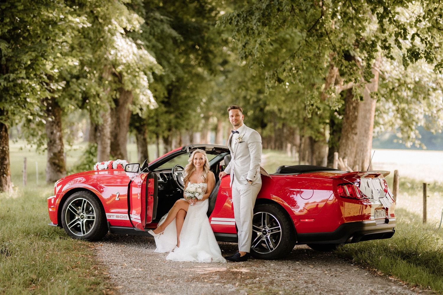 A red sports car parked along a scenic tree-lined path.