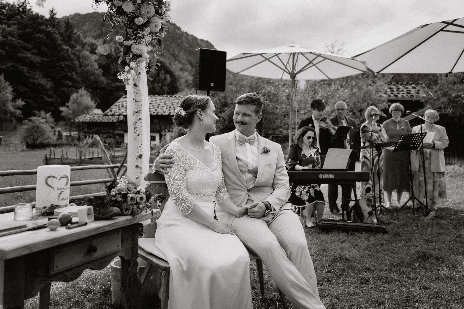 Wedding celebration under white umbrellas with mountains and trees creating a natural backdrop.