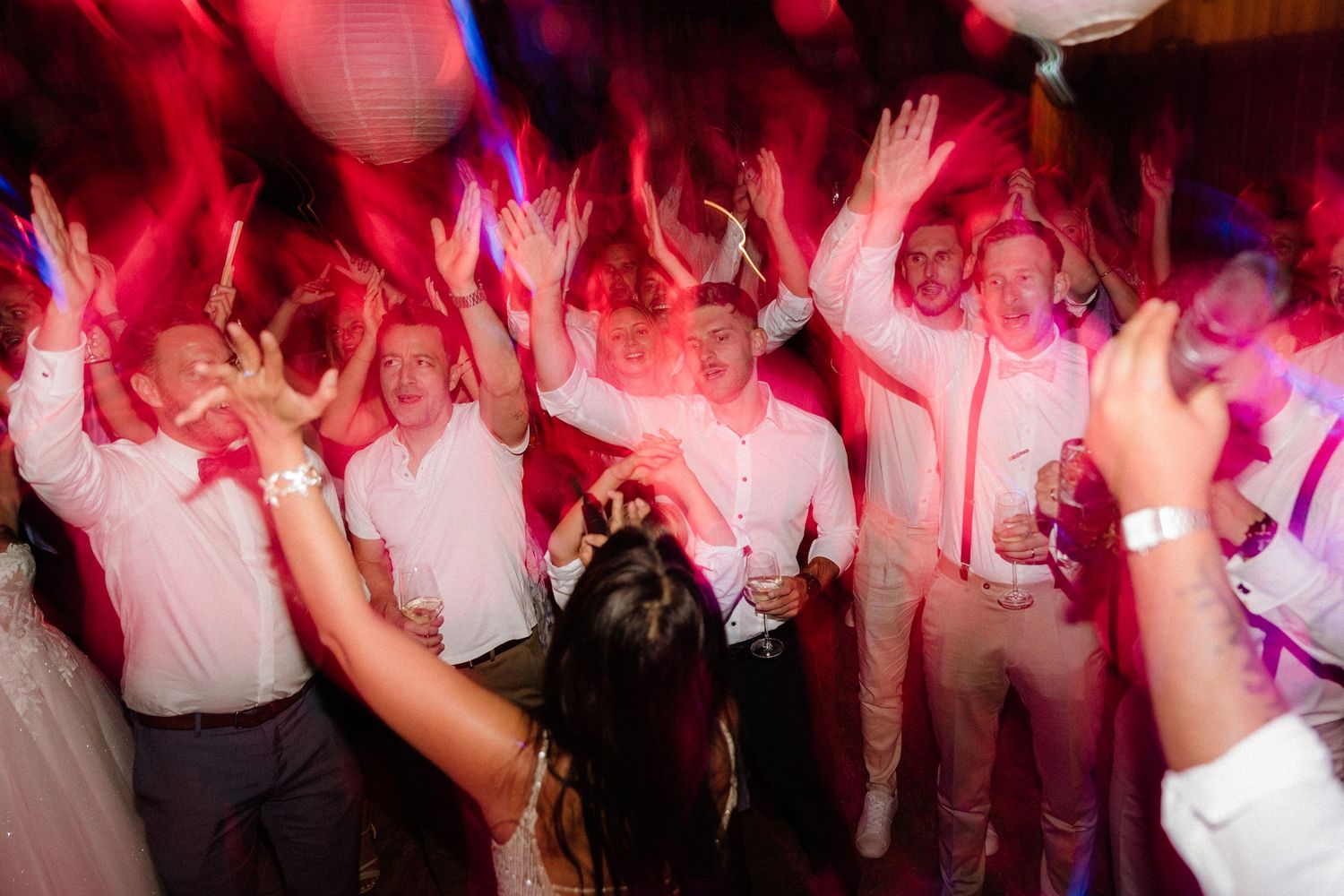Crowded dance floor at wedding reception illuminated by red mood lighting.