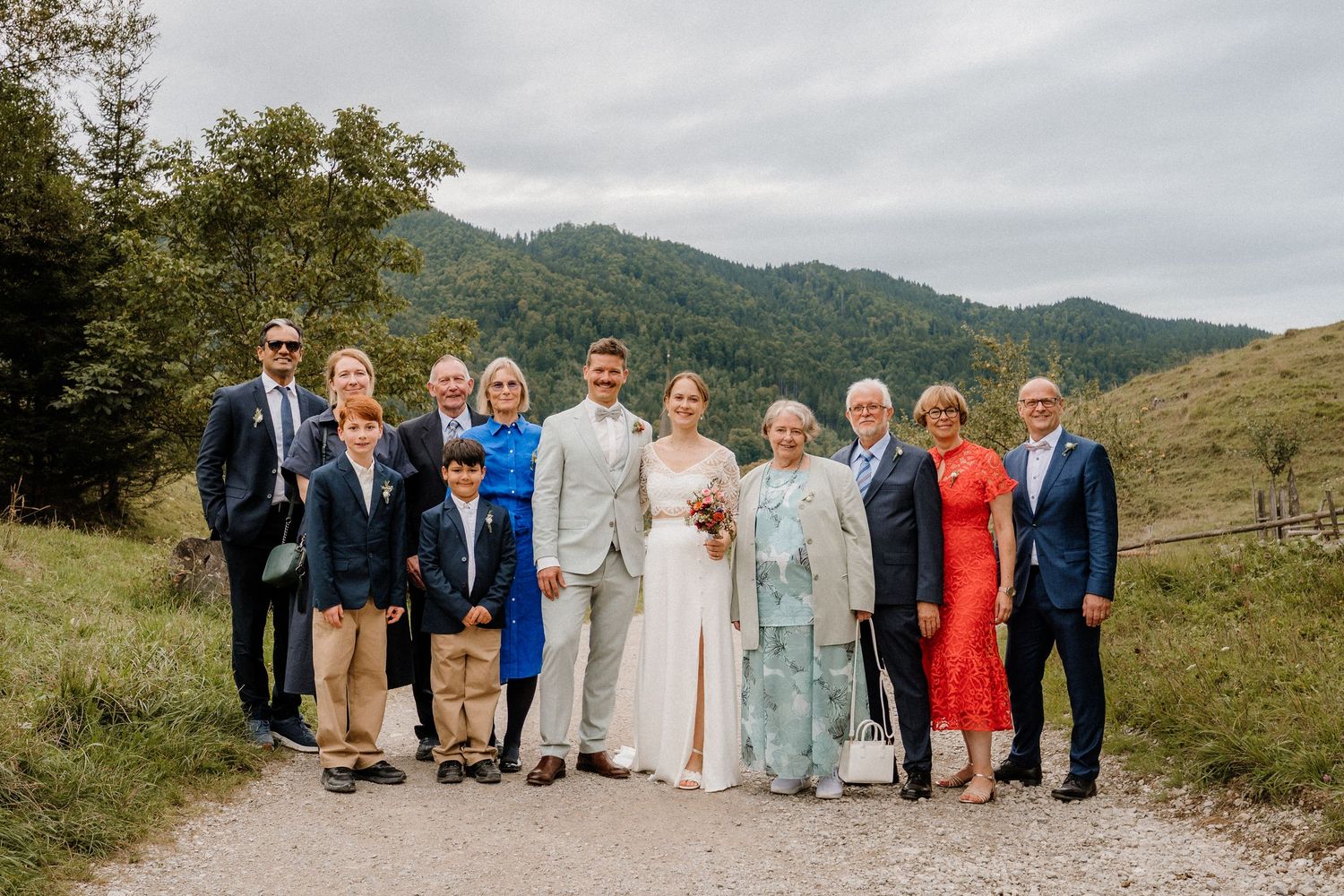 Panoramic wedding party photo with mountains and cloudy sky in the background.