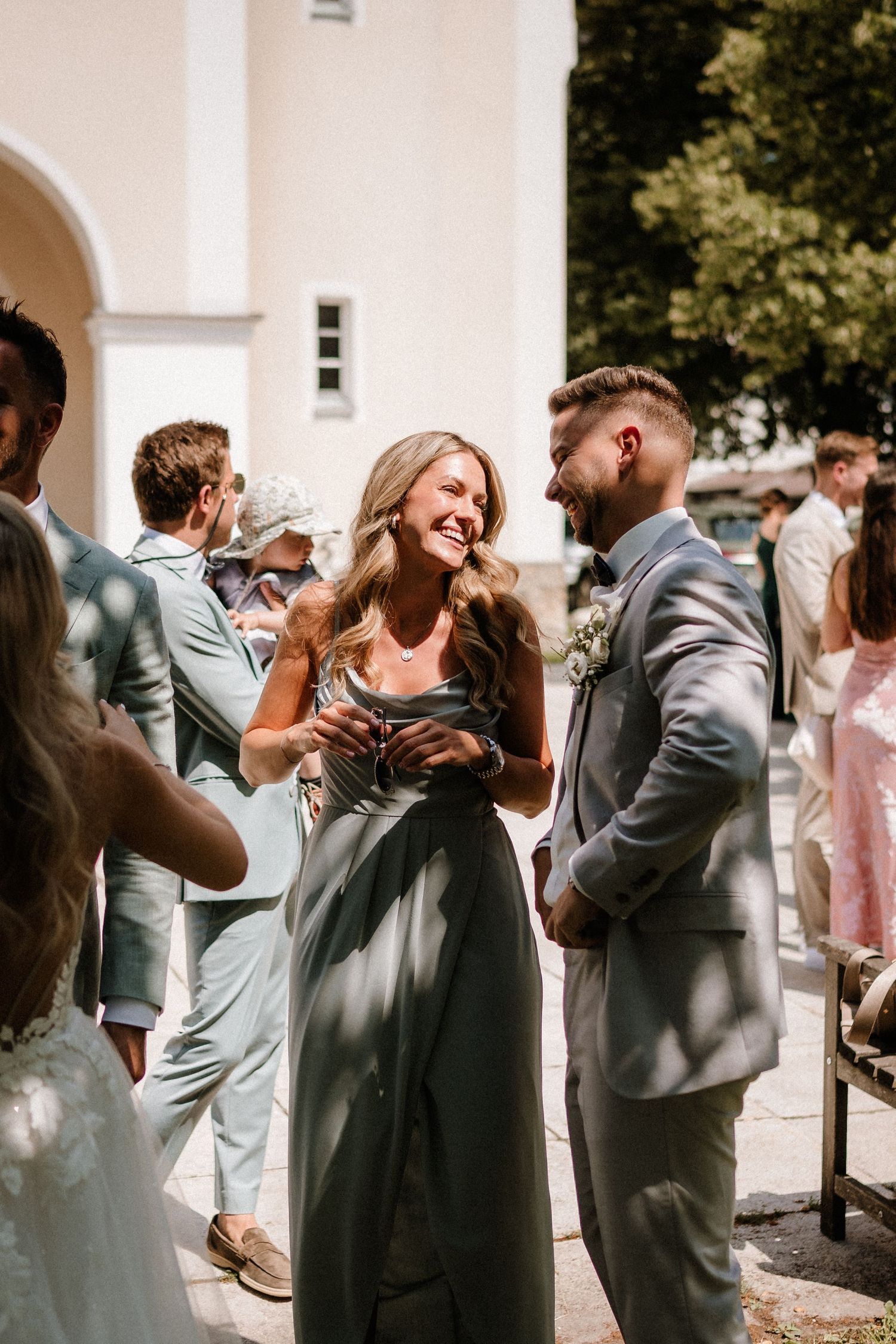 Wedding guests in formal attire share laughs during outdoor reception.
