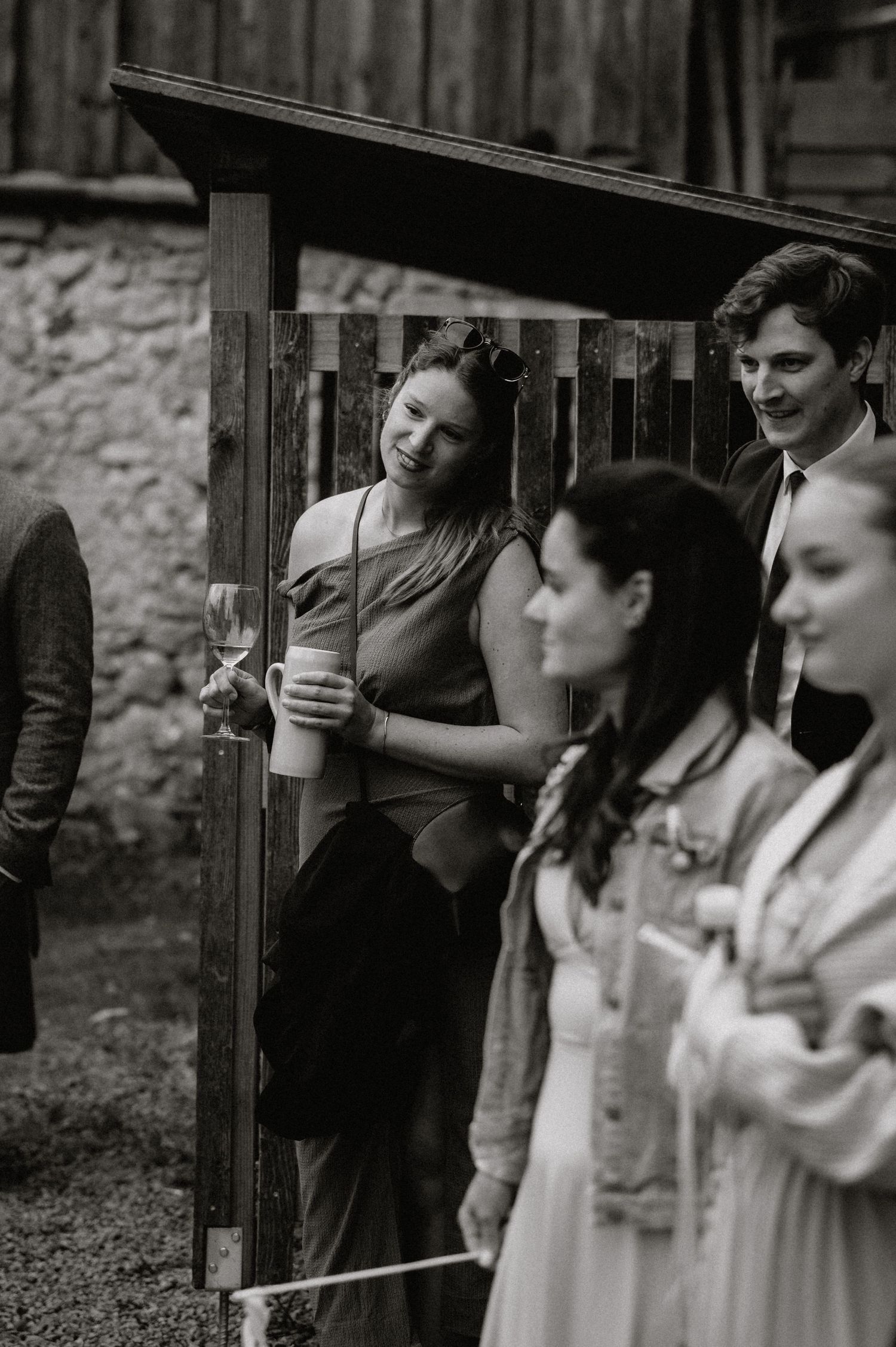 Wedding guests participate in a traditional log sawing ceremony outside a rustic wooden building.