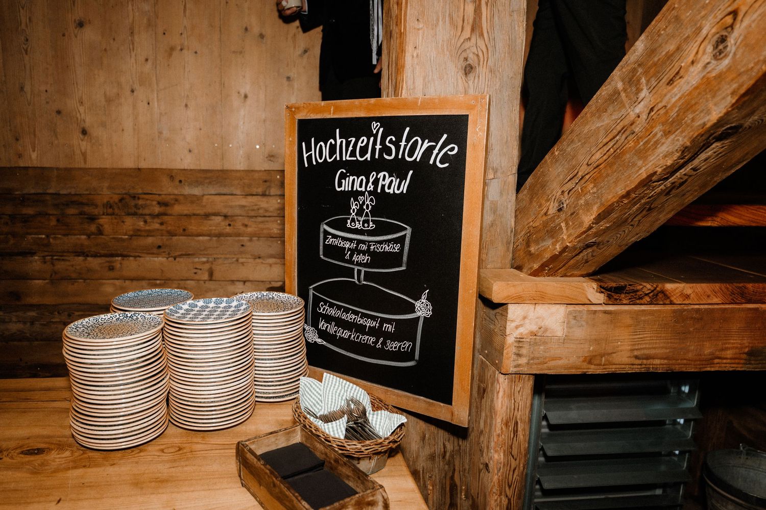 Wooden interior of a rustic venue with stacked plates and chalkboard menu signs.