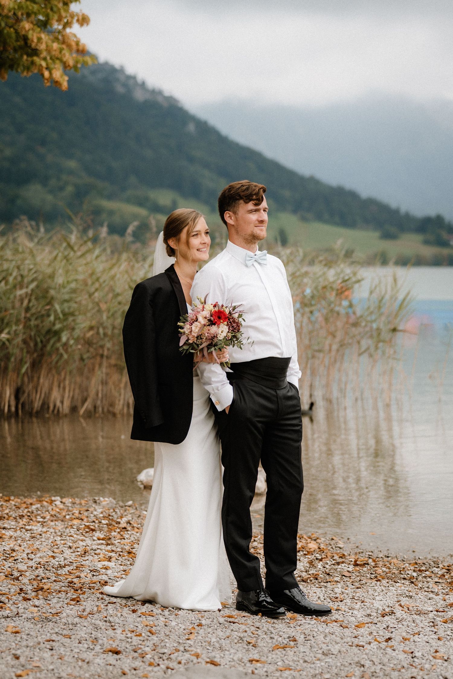 Wedding couple sitting by a lake with mountains and autumn foliage in the background.