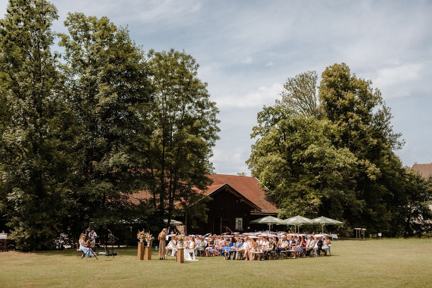 Outdoor wedding ceremony setup with wooden chairs arranged in rows on a grassy lawn under tall trees.