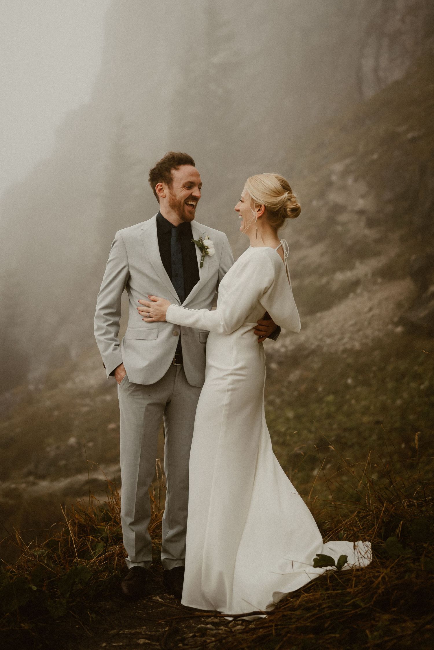 Bride and groom share a joyful moment together in the misty mountain landscape.