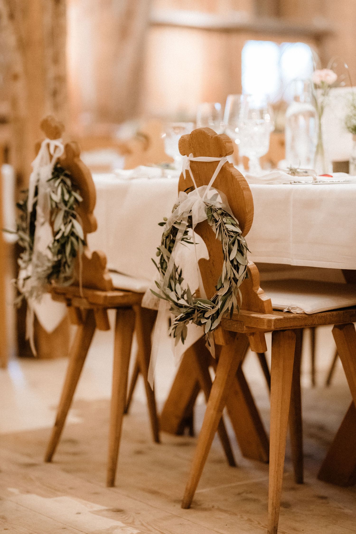Wooden chairs decorated with olive branch garlands at a rustic wedding reception.