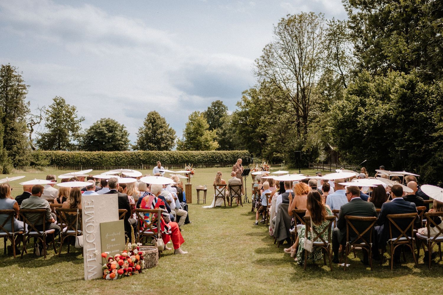 Wide angle view of outdoor wedding reception with white tents and chairs on a lawn.