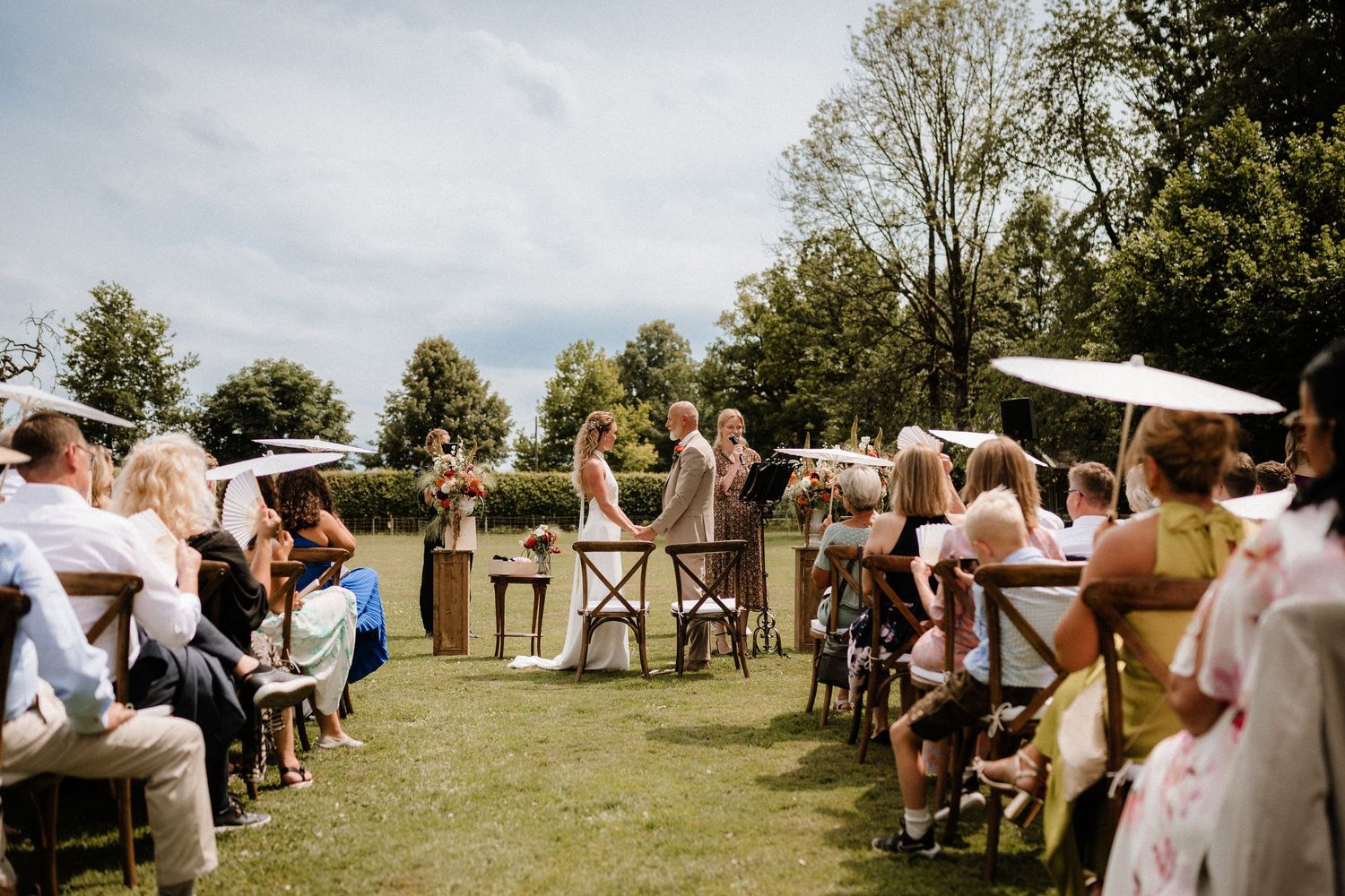 Wedding guests gather on a sunny lawn with a white church steeple visible in the background.