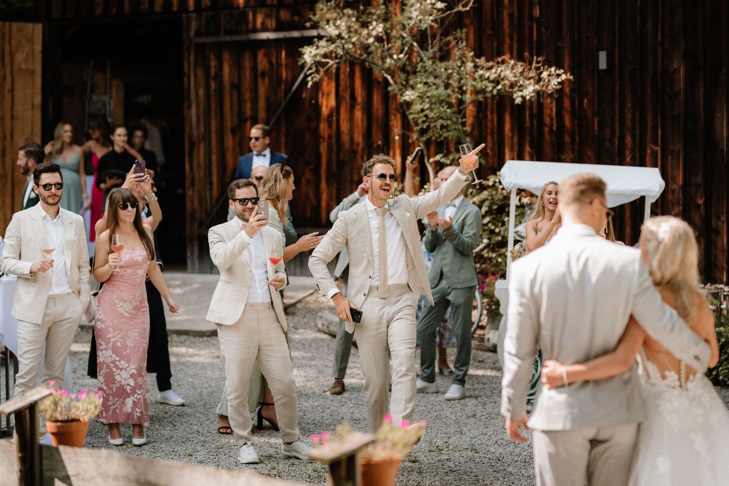 Wedding guests celebrate on a rustic barn pathway lined with wooden walls.