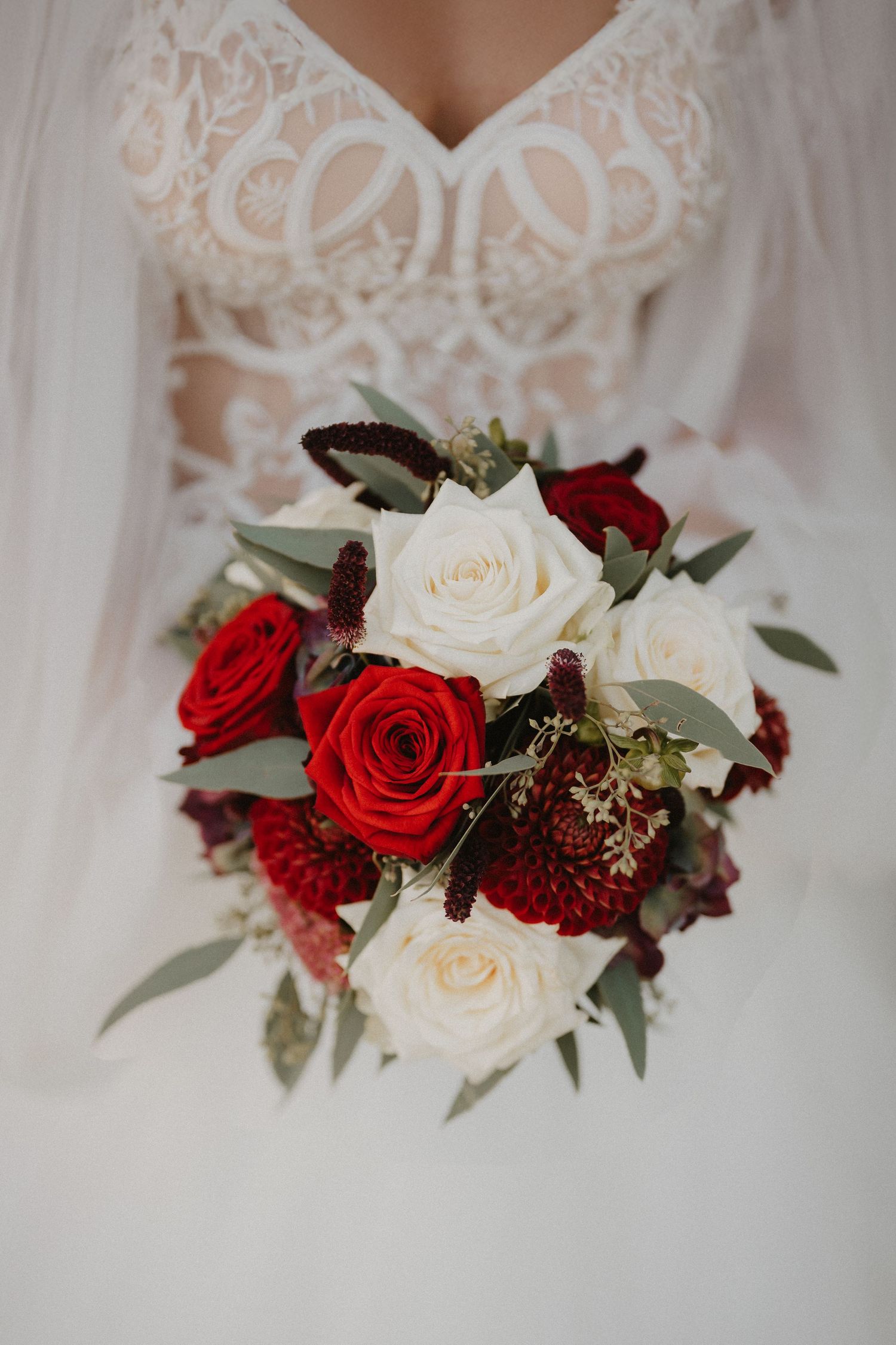 Close-up of a bridal bouquet featuring red and white roses with greenery accents.