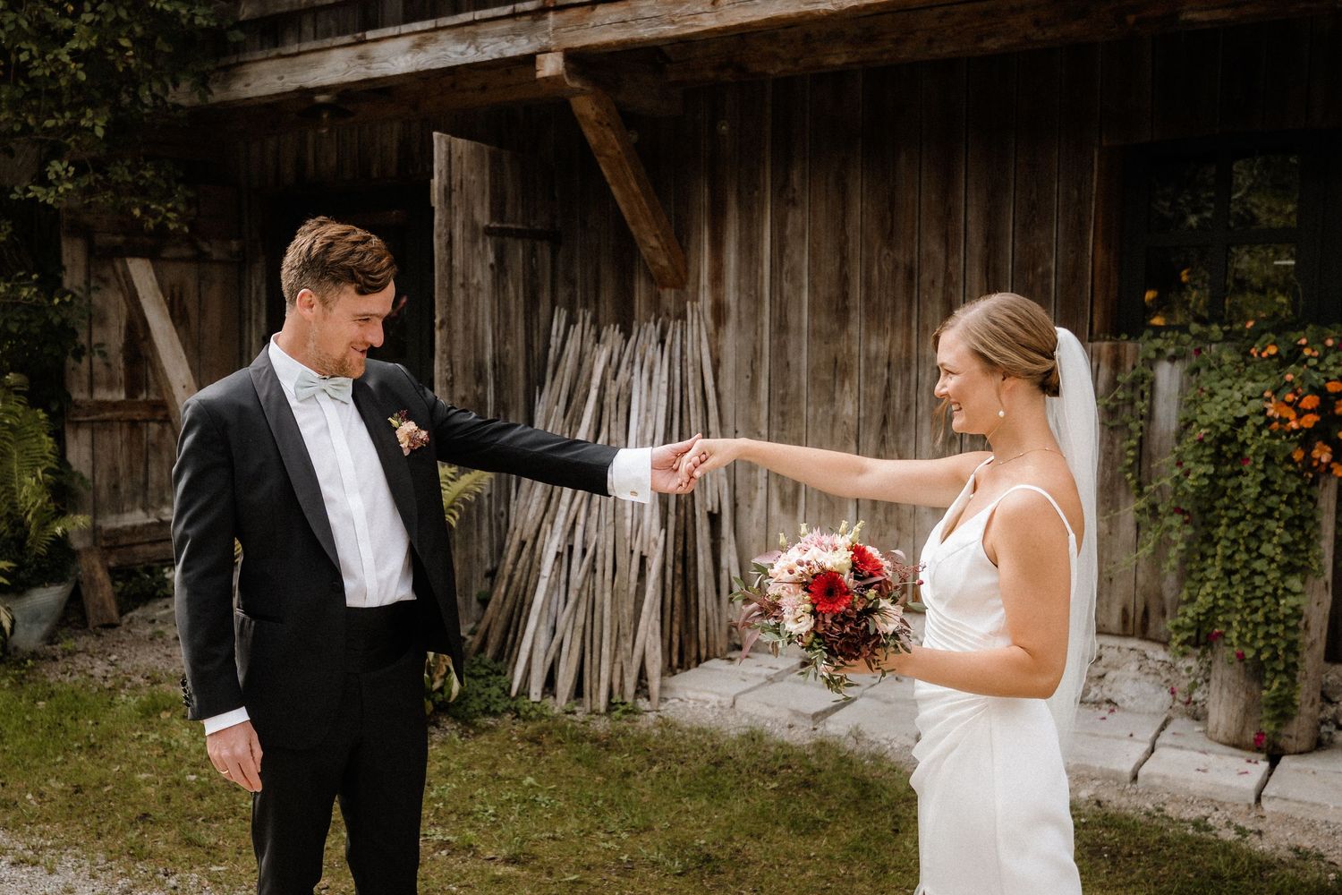 A couple in wedding attire shares a romantic moment in front of a rustic barn setting.