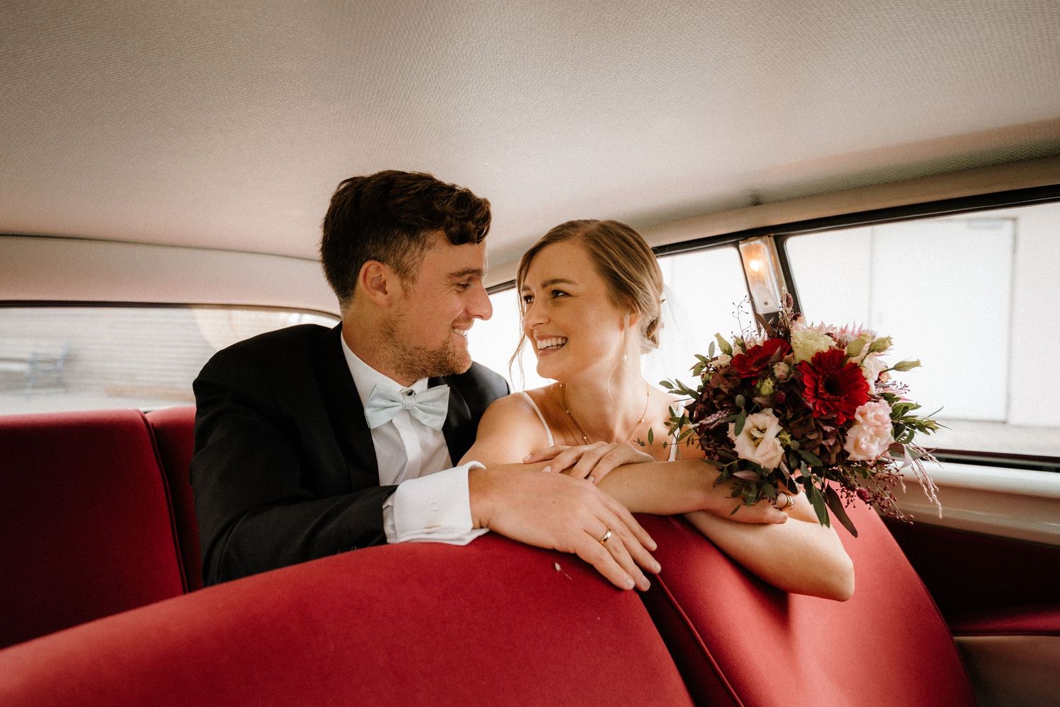 Romantic couple shares tender moment in classic car with red leather interior.
